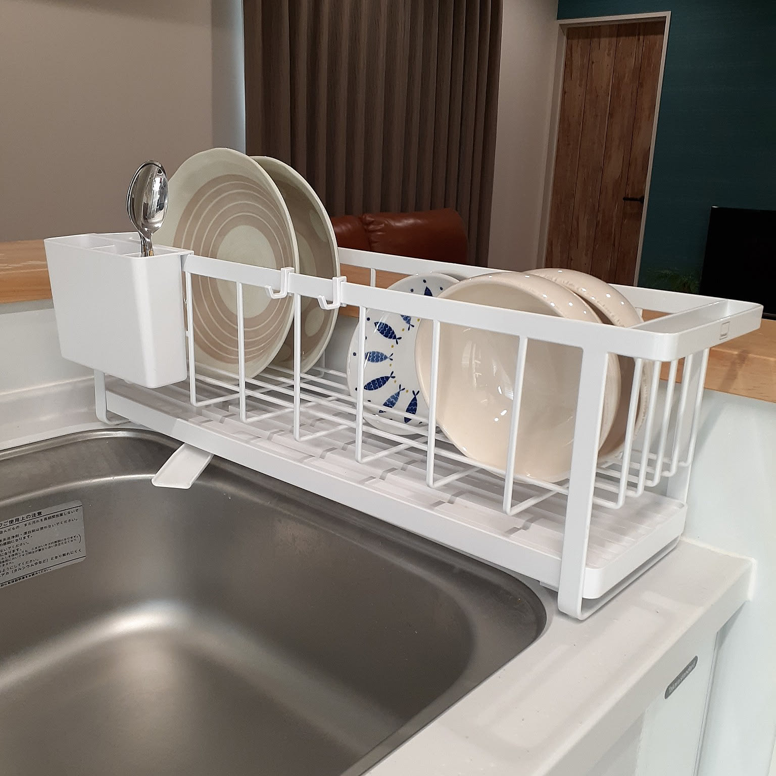 A white Yamazaki dish rack with a removable drain tray holding plates over a kitchen sink.