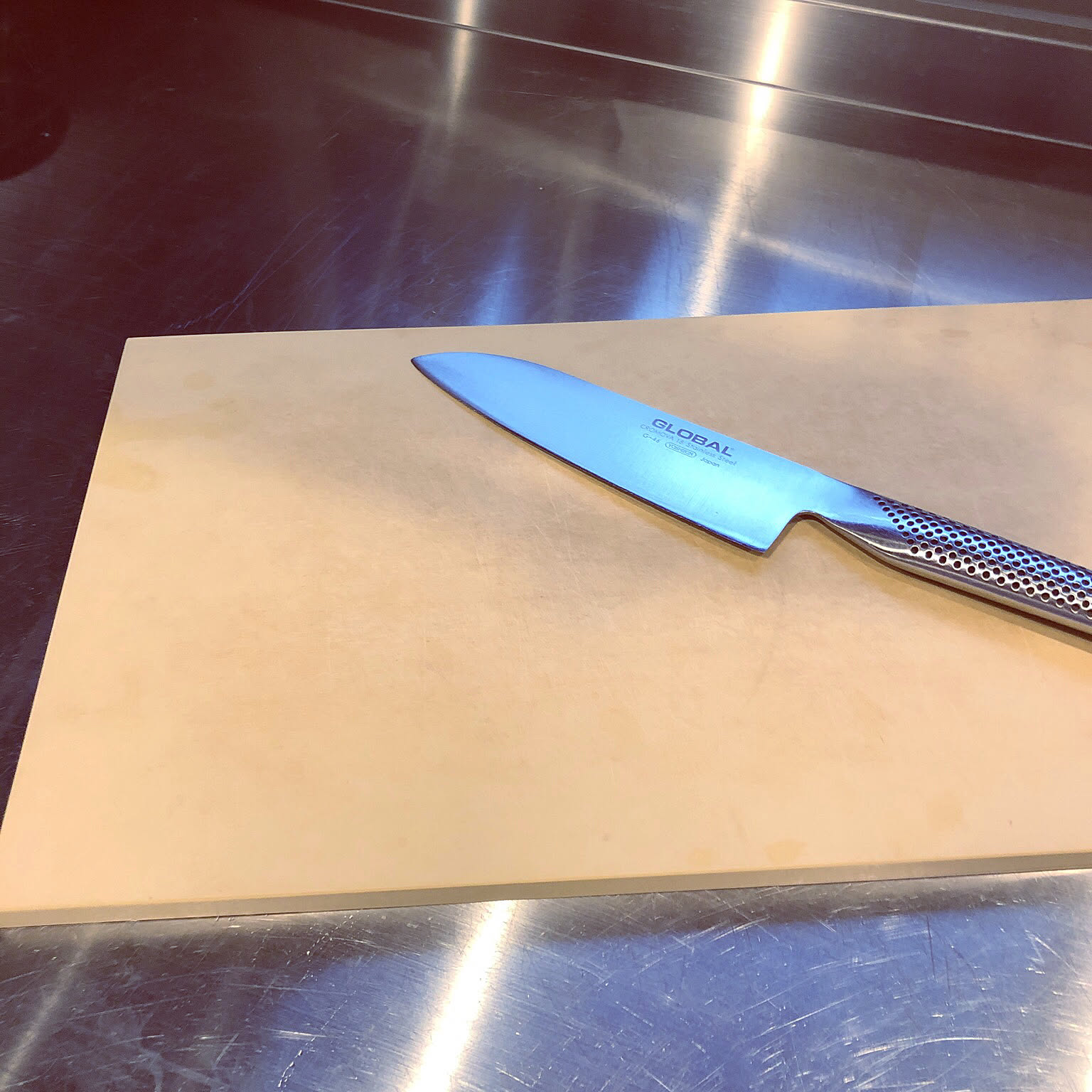 Global Japanese kitchen knife on a large light-colored cutting board.