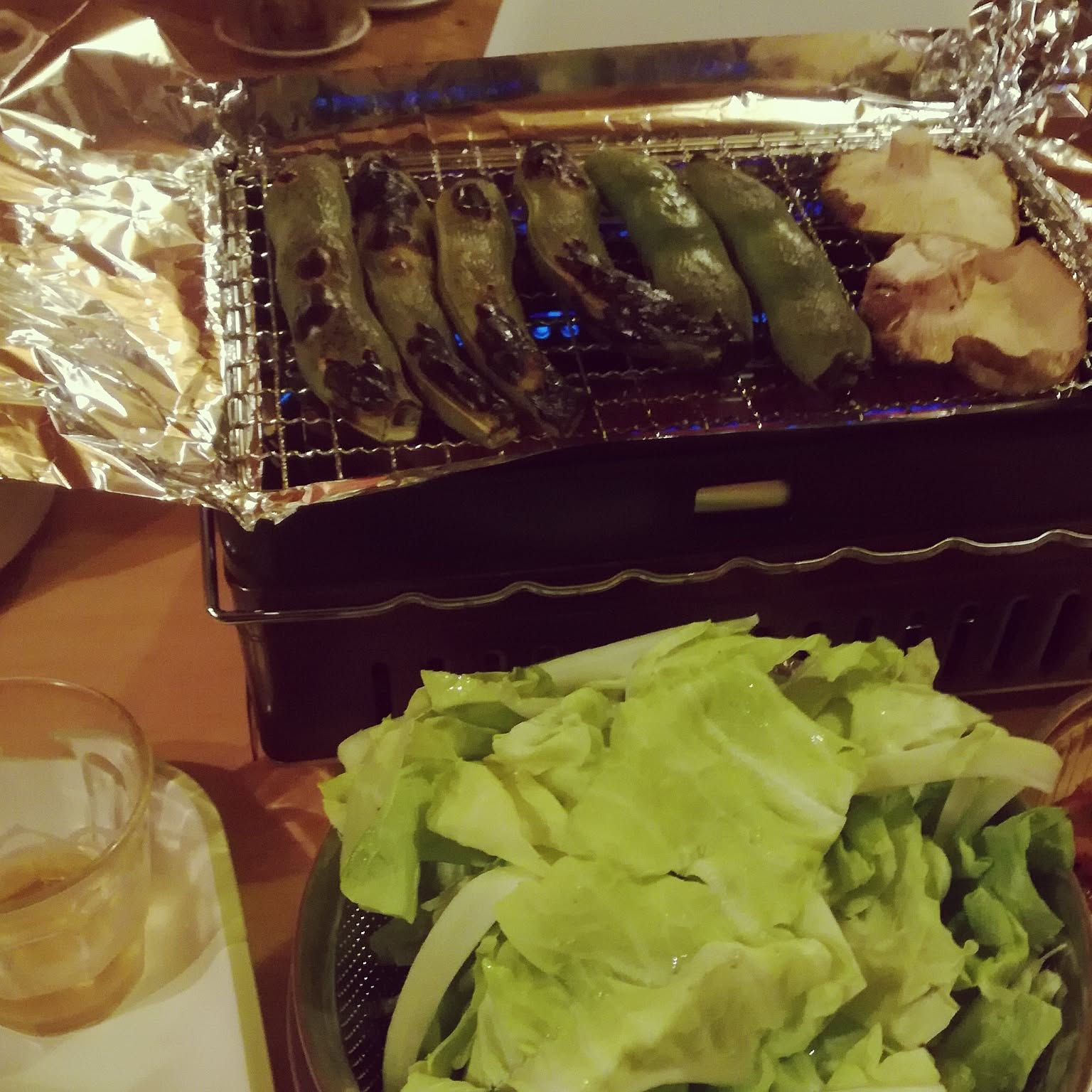 An Iwatani Aburiya robata grill cooking vegetables on a close-up tabletop grate.