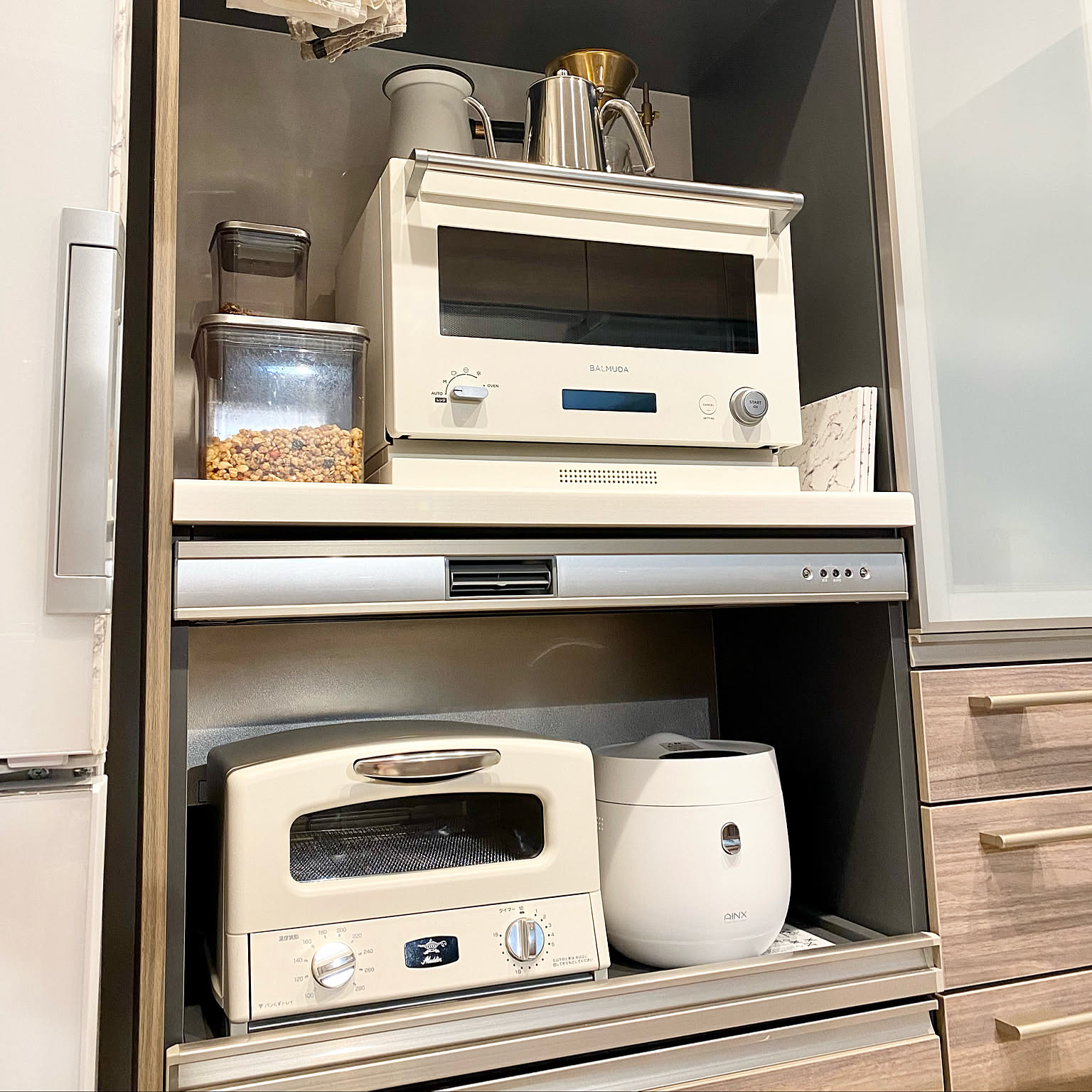 A compact white rice cooker stored in a neat kitchen appliance shelf.