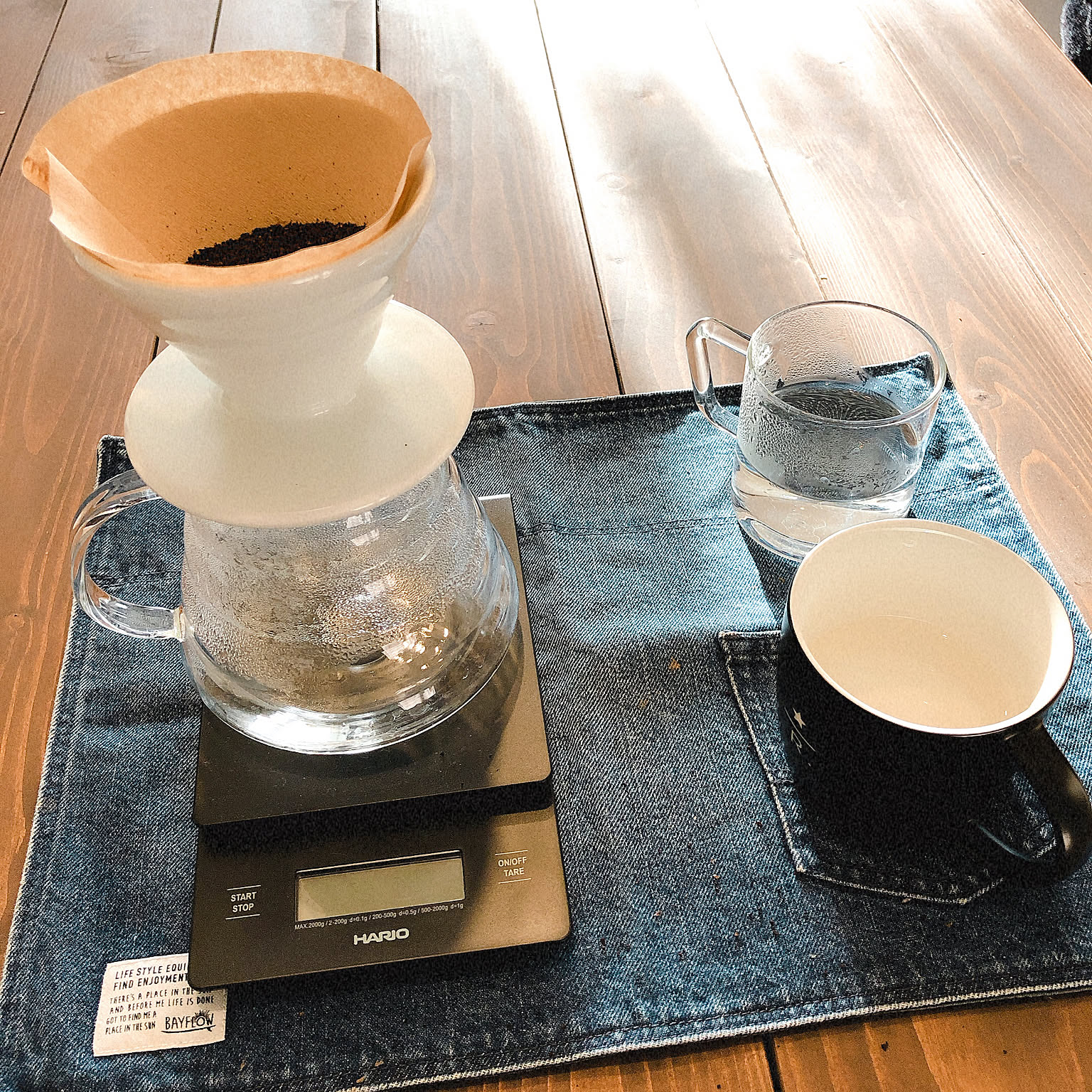 A white HARIO V60 ceramic dripper brewing coffee into a glass server on a scale.