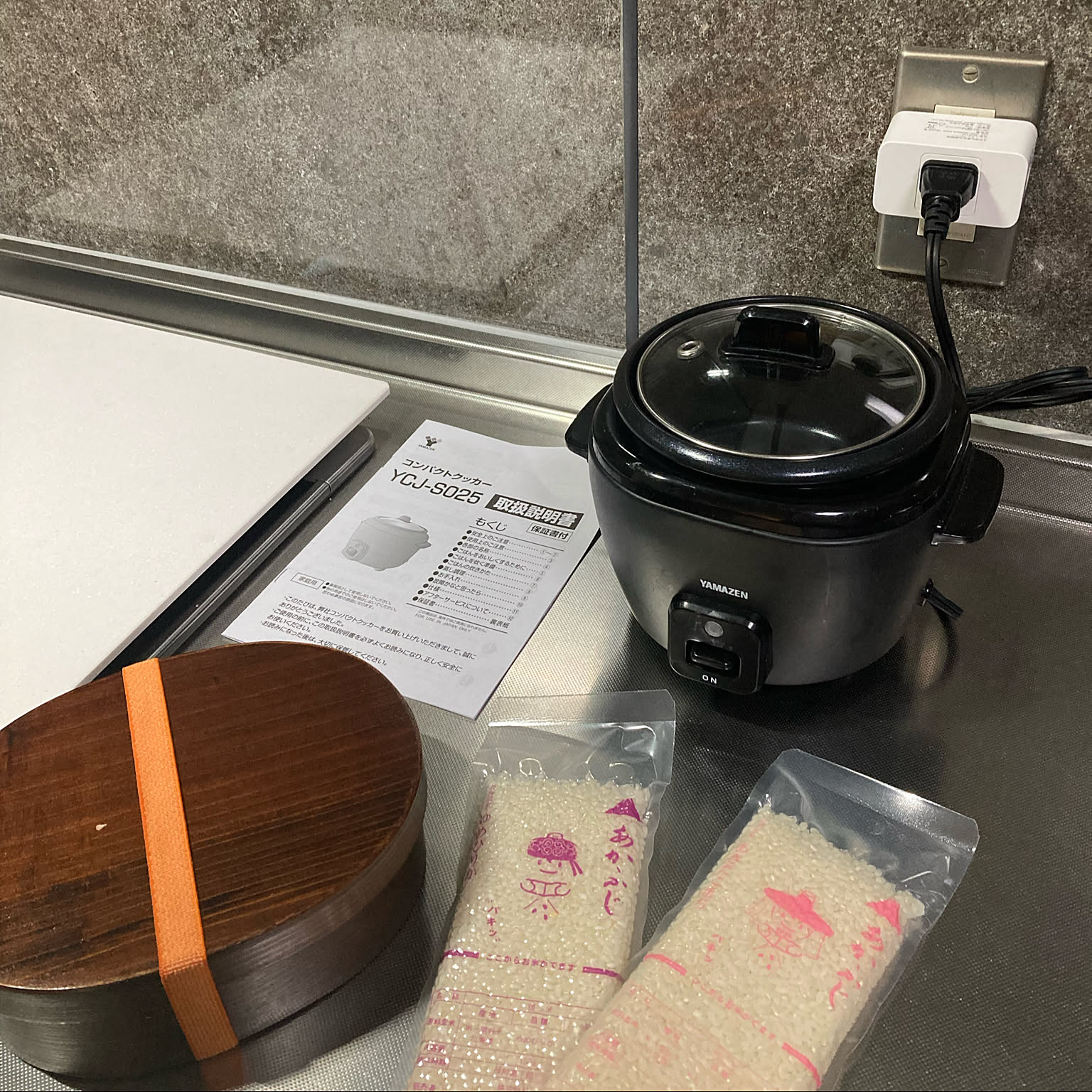 A black compact Yamazen cooker set on a counter with rice portions and a lunch box.