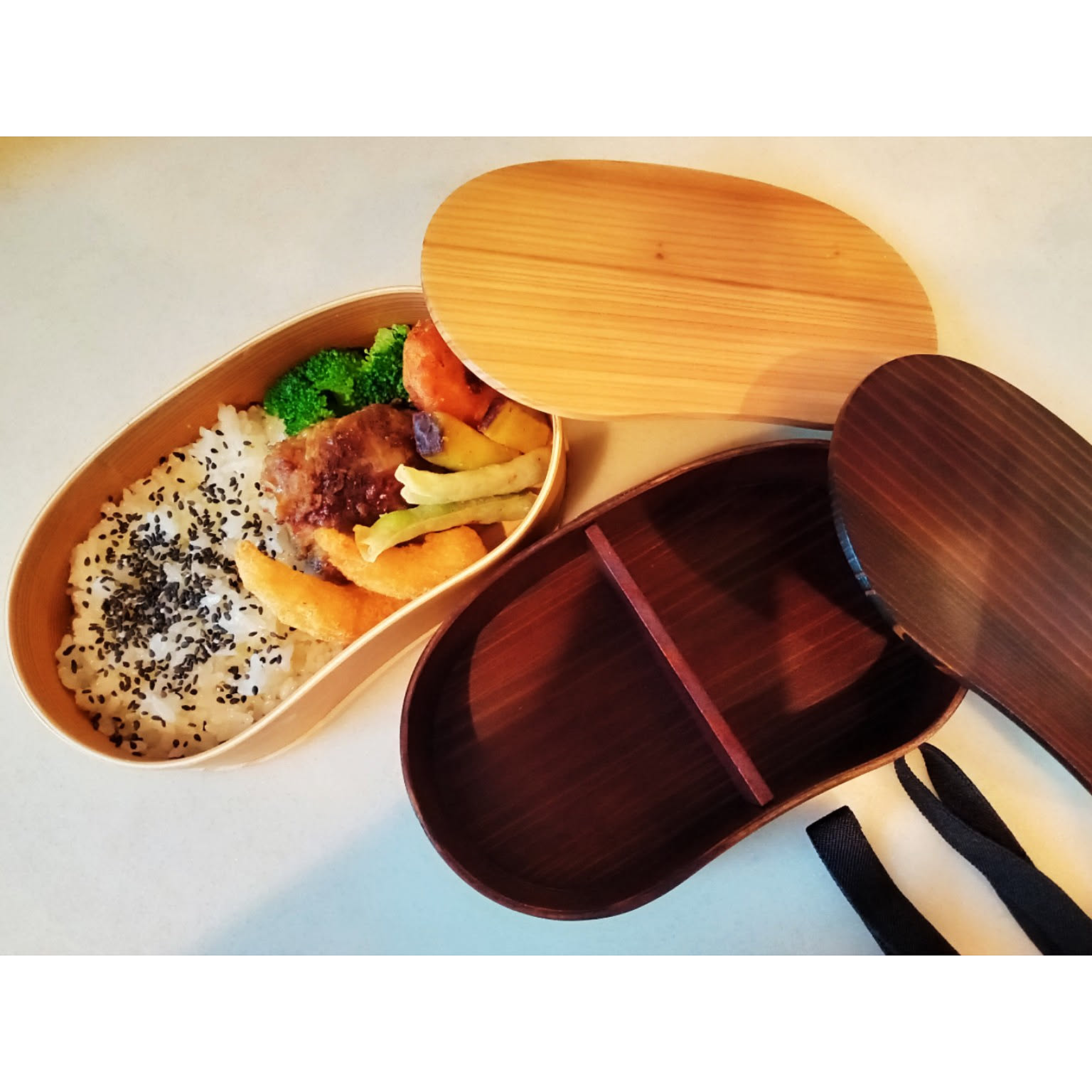 Natural and dark-finished wooden magewappa bento boxes, one packed and one empty with its lid open.