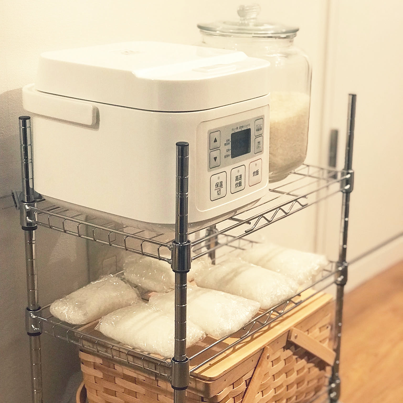 A compact white 3-cup rice cooker stored on a small metal rack with a rice jar.