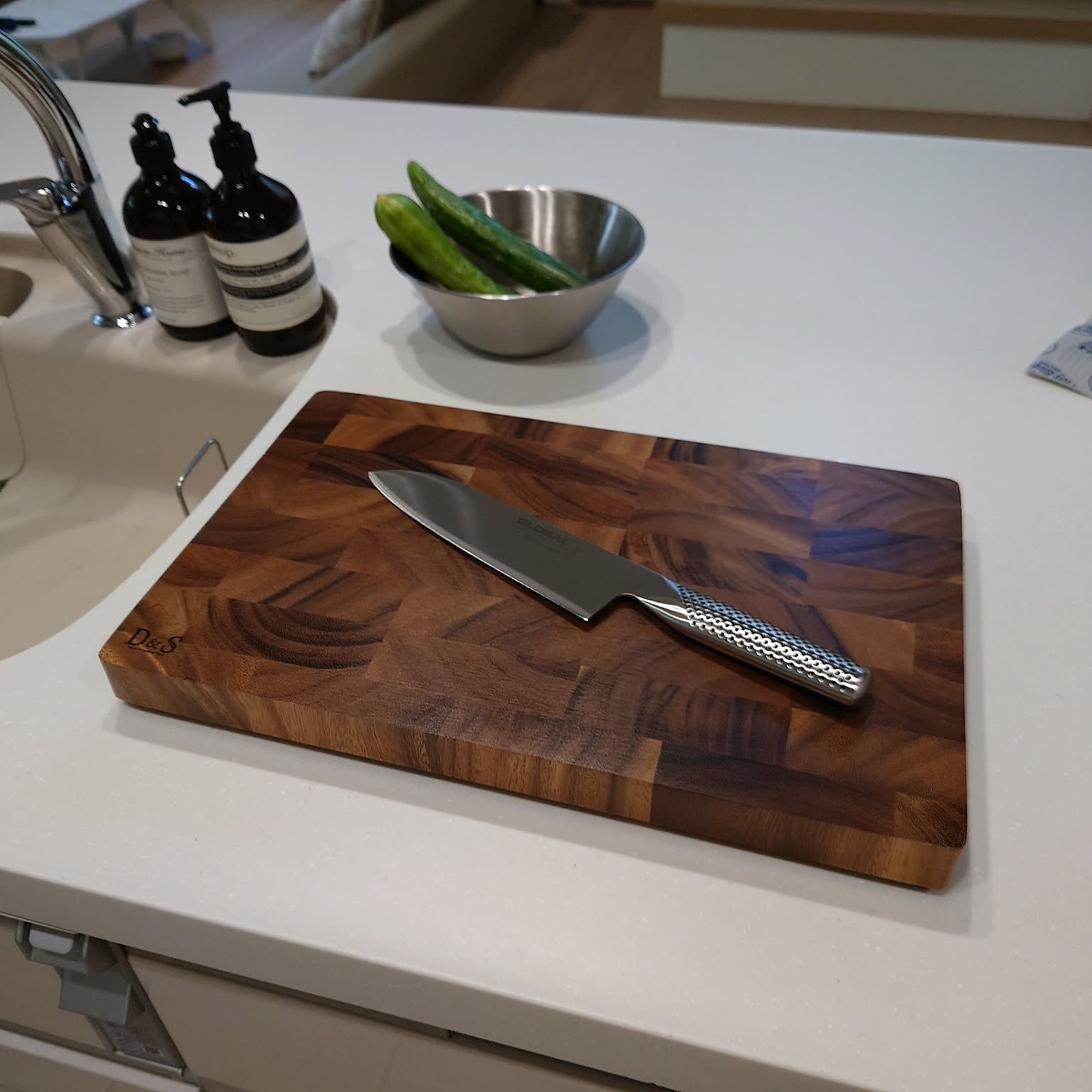 Japanese kitchen knife resting on a thick wooden cutting board beside vegetables.
