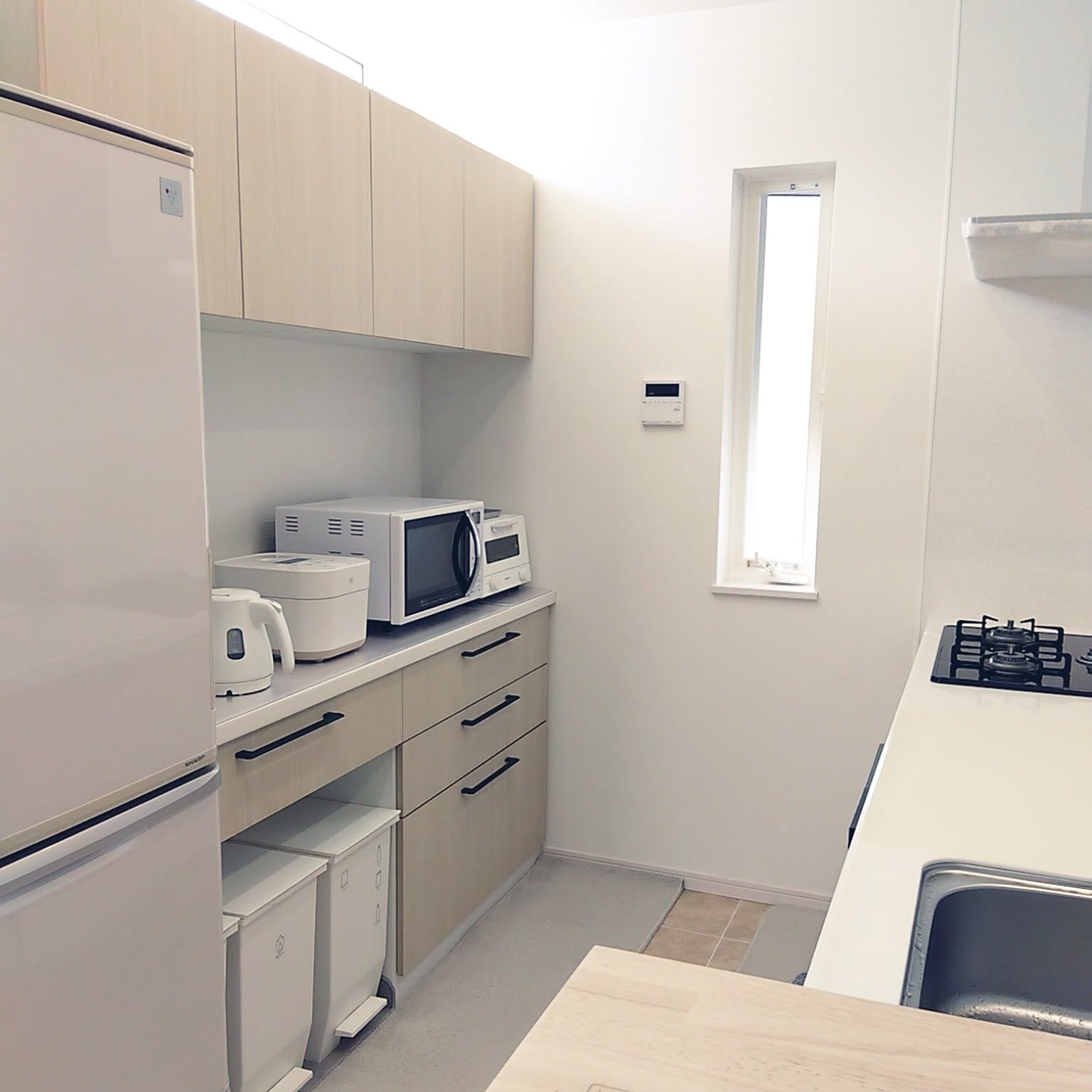 A bright white Japanese kitchen with small appliances arranged along one side and a clear counter kept open for cooking and cleaning.