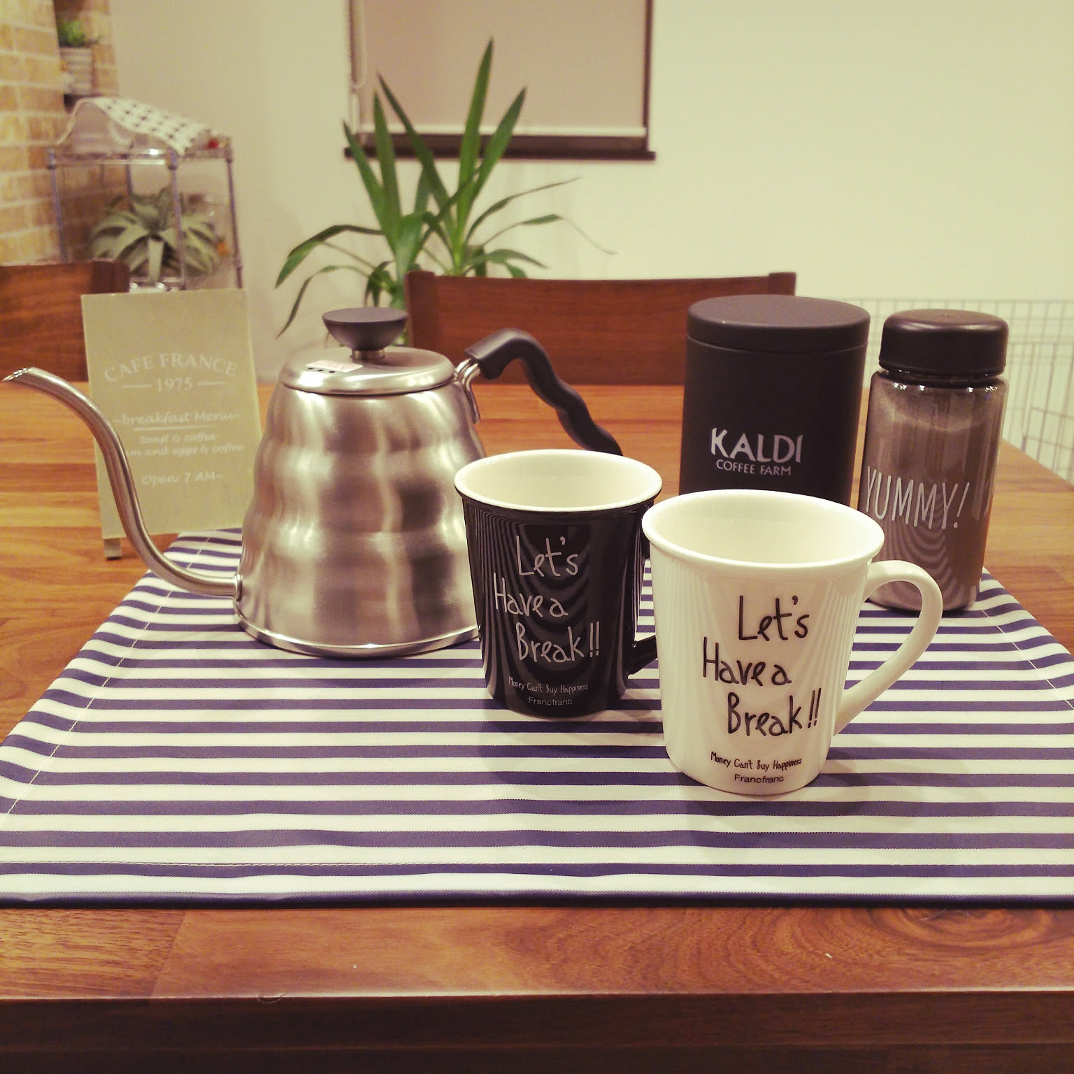 A HARIO Buono-style gooseneck kettle set on a coffee tray with mugs and coffee storage.