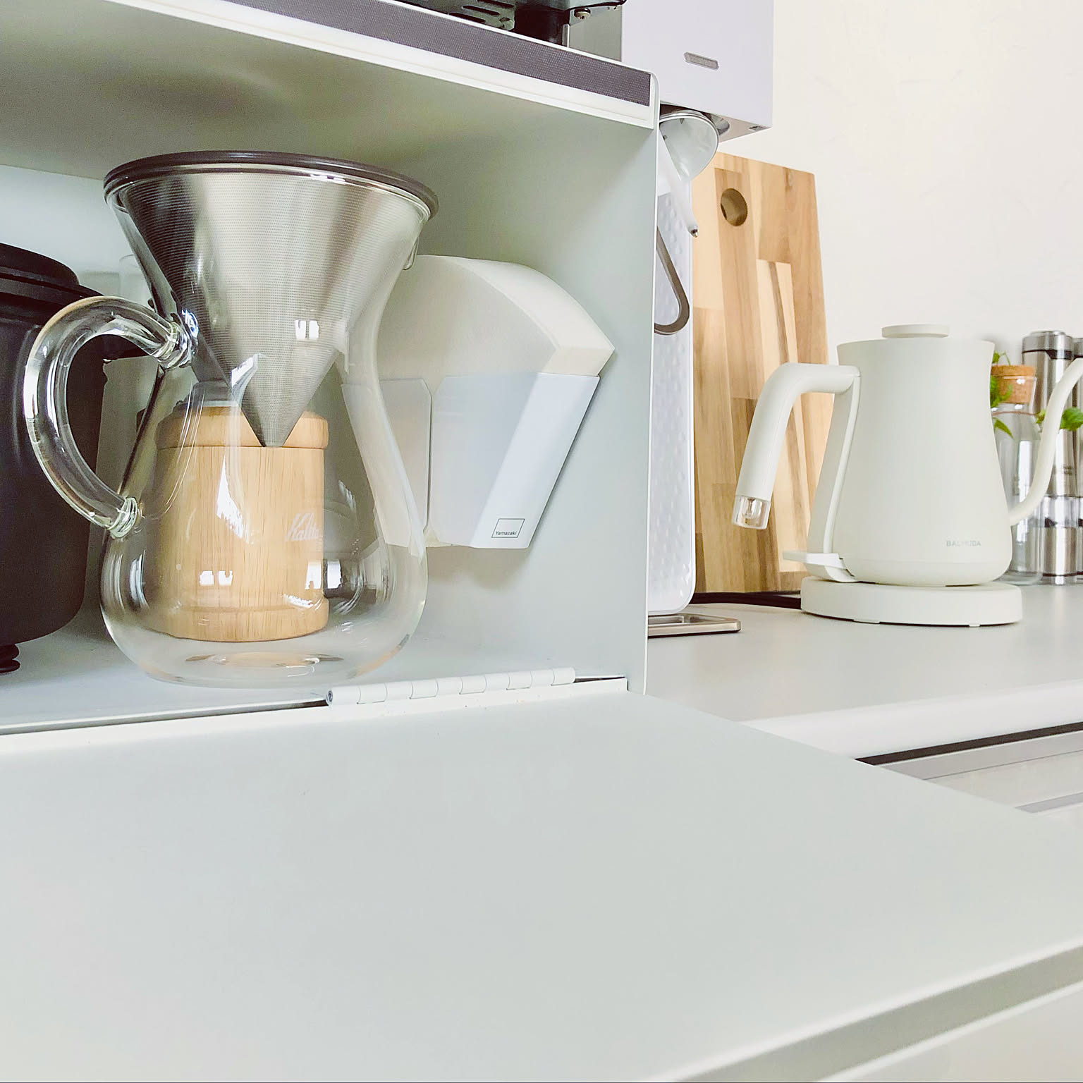 Coffee carafe, white kettle, and magnetic filter holder beside a compact counter shelf.