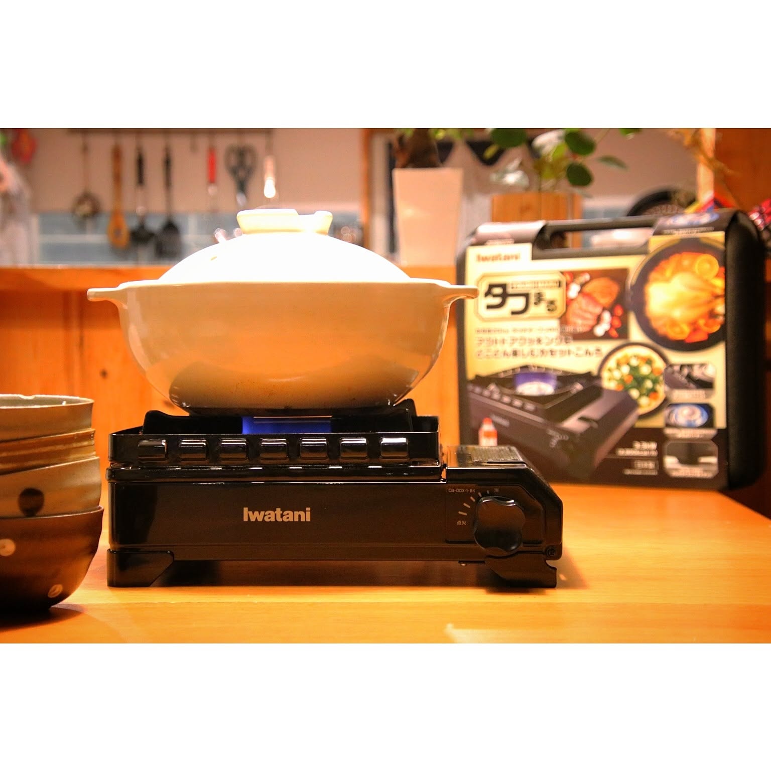 An Iwatani Tough Maru cassette stove cooking with a pot, shown with its box behind it.