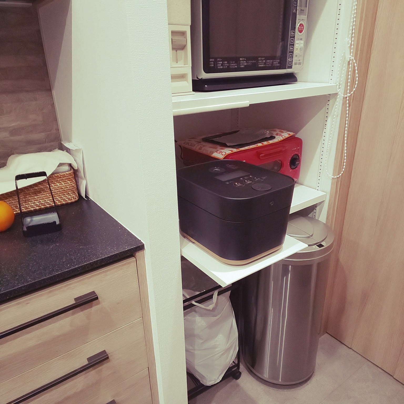 A black rice cooker stored on a pull-out shelf in a compact appliance cabinet.