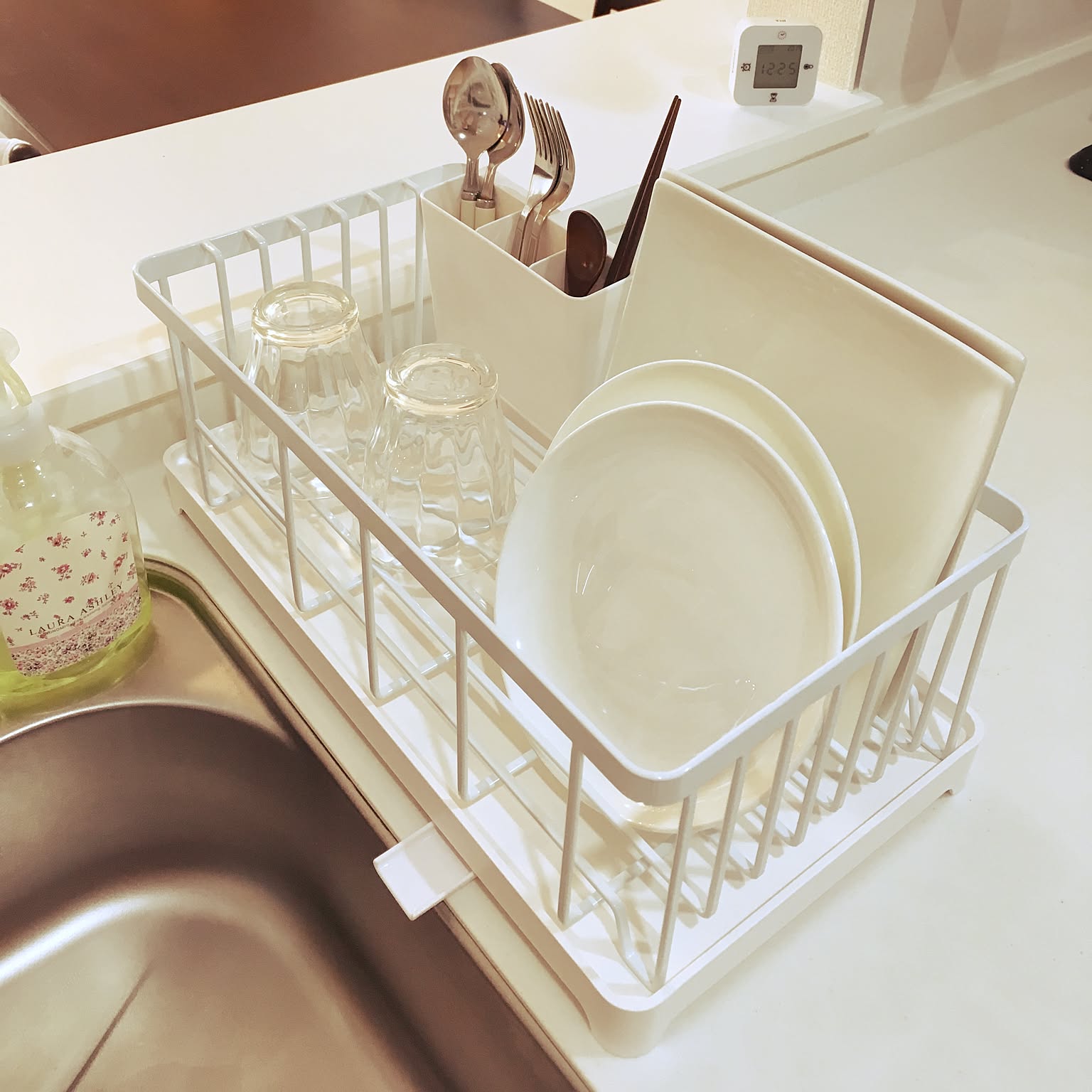 A compact white Yamazaki Tower wire dish rack holding plates, glasses, and utensils on a kitchen counter.