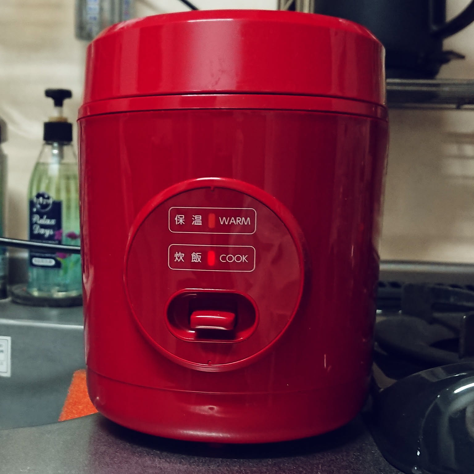 A red Yamazen 1.5-go mini rice cooker shown close-up in a narrow kitchen.