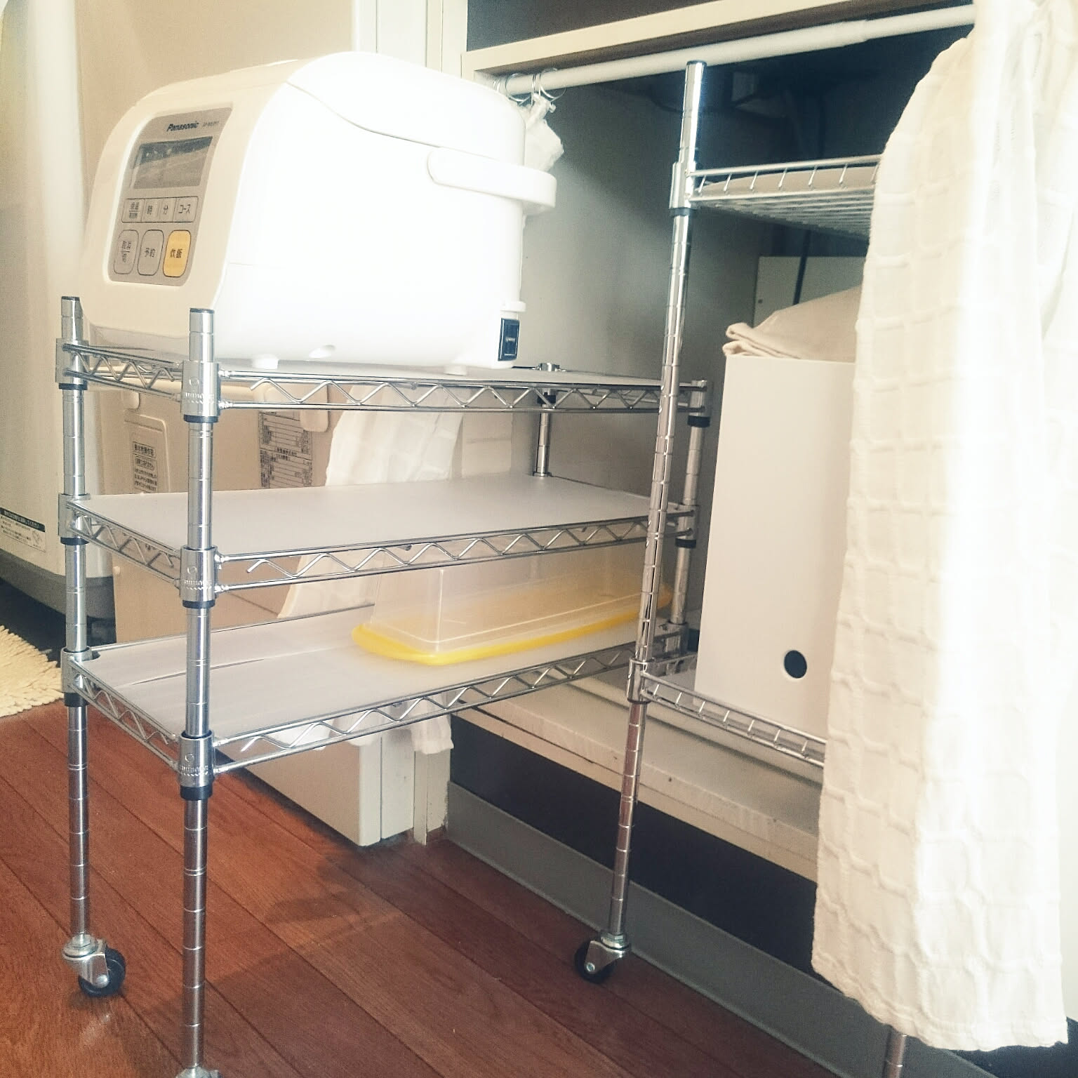 A small white rice cooker on a rolling rack tucked under a compact kitchenette.