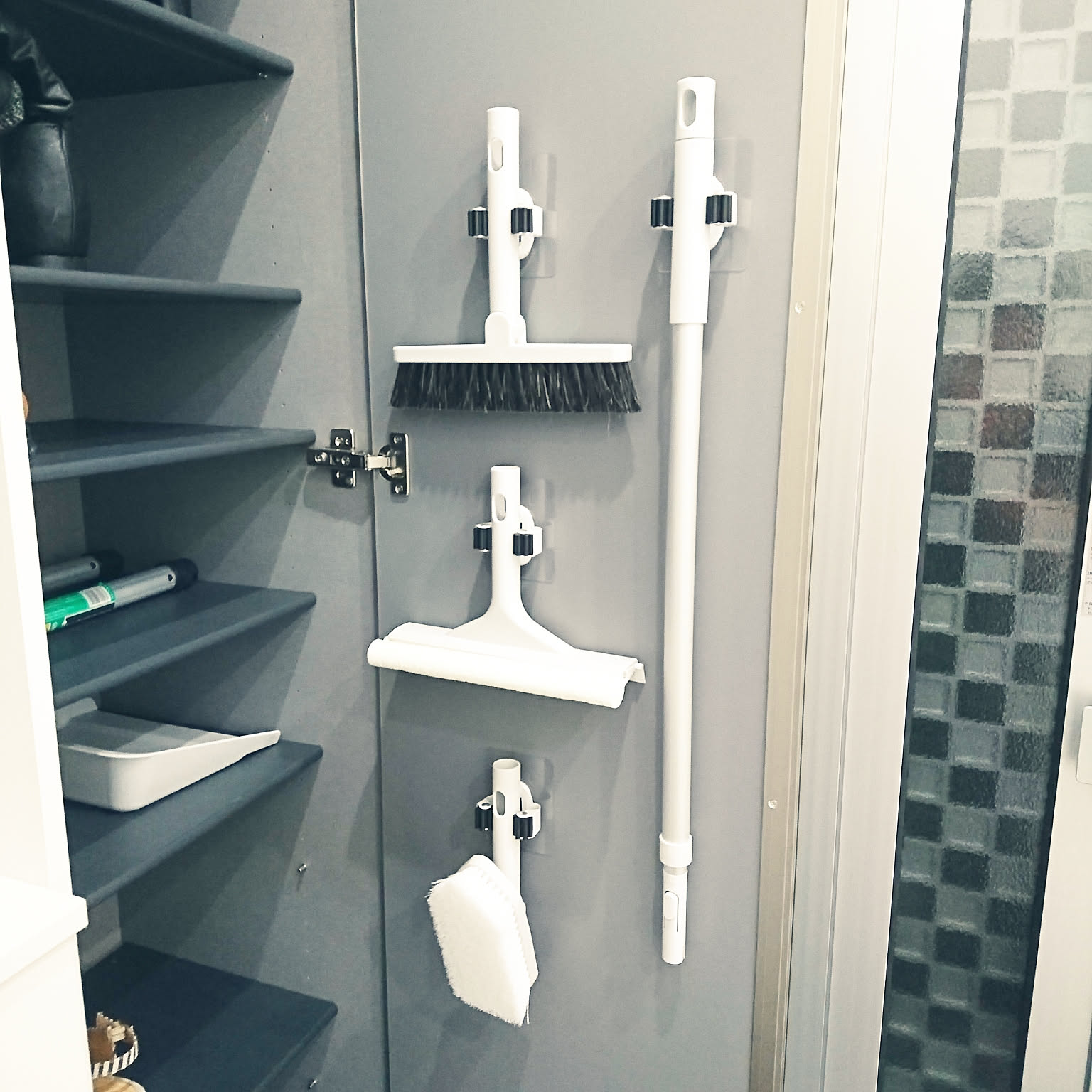 Cleaning tools mounted inside a shoe cabinet door beside shoe shelves.