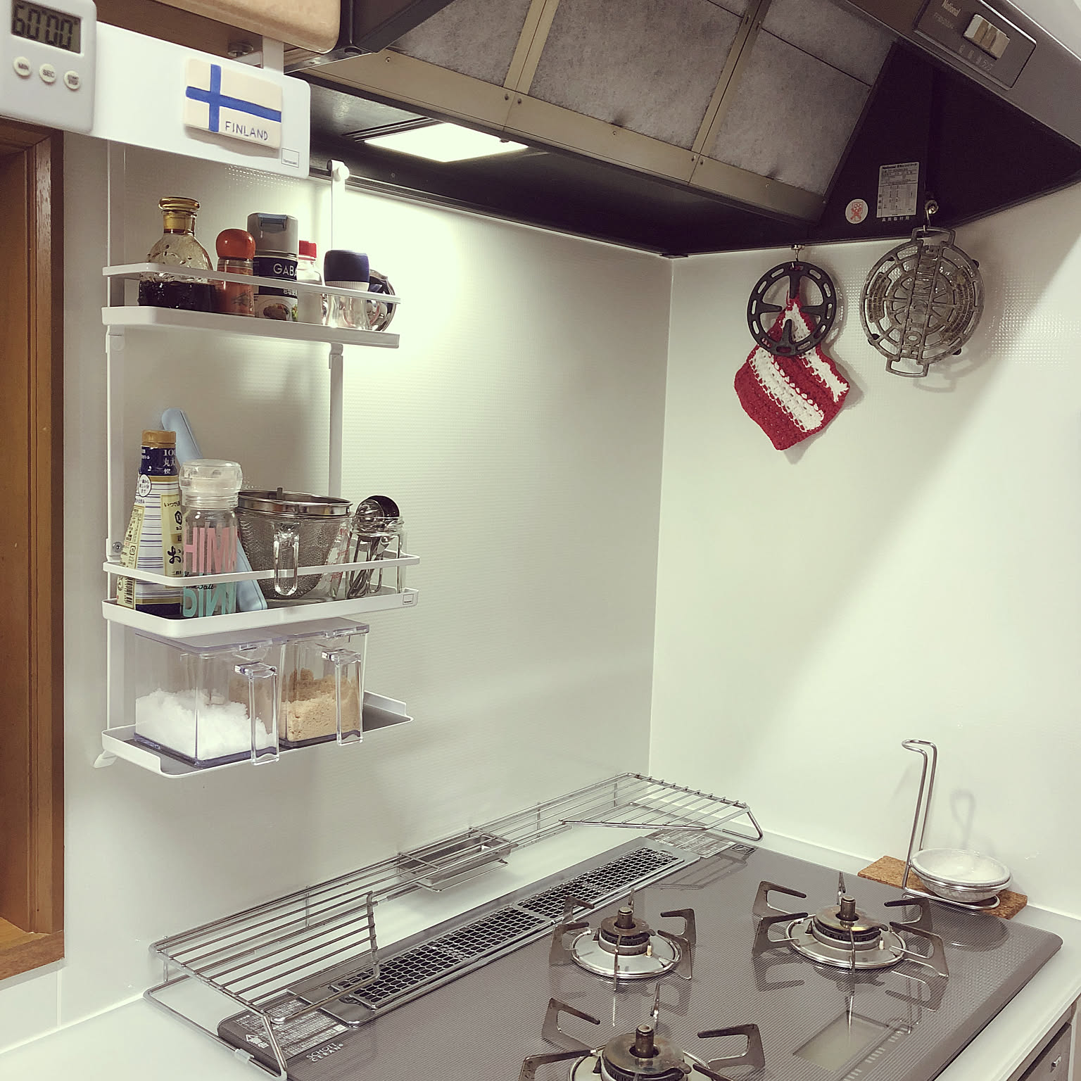 A Yamazaki Tower range hood spice rack holding bottles and seasonings above a clean gas cooktop.