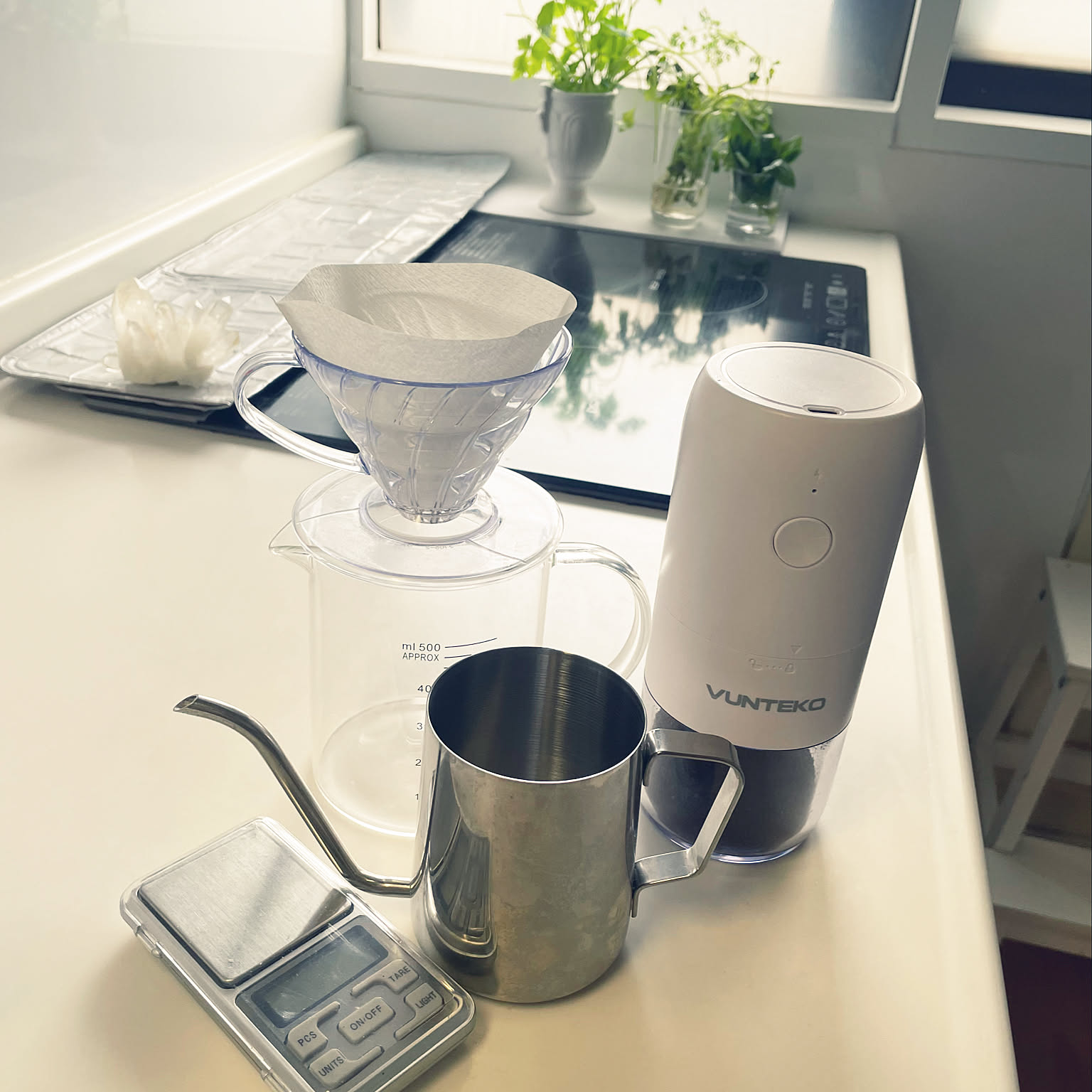 A clear HARIO V60-style dripper, paper filters, grinder, and measuring tools stored together on a kitchen wall.