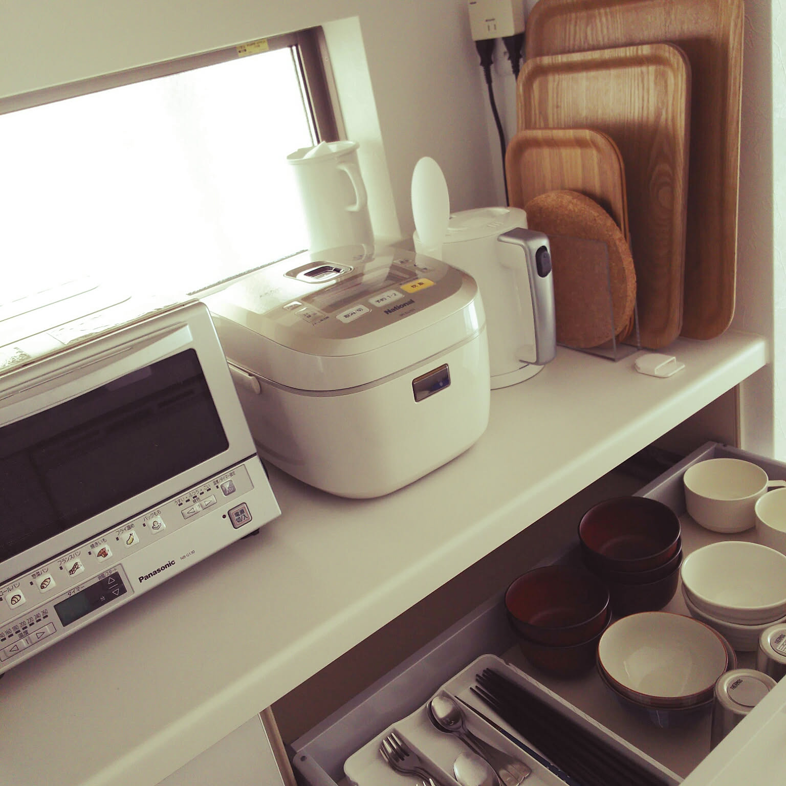 A rice cooker placed on a kitchen counter near everyday serving items.