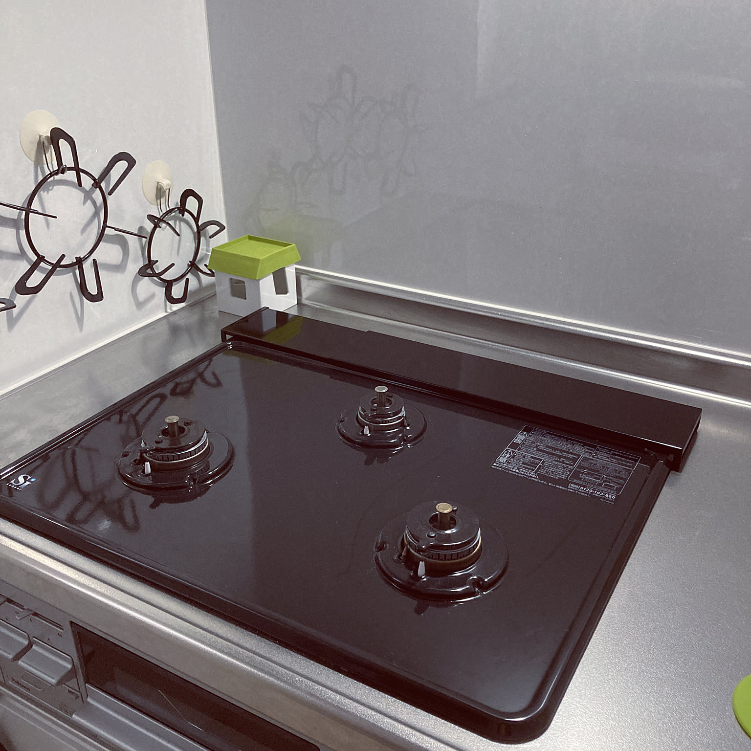 A black steel exhaust vent cover sitting over the slot at the back of a Japanese gas stove, with the glossy black cooktop in front