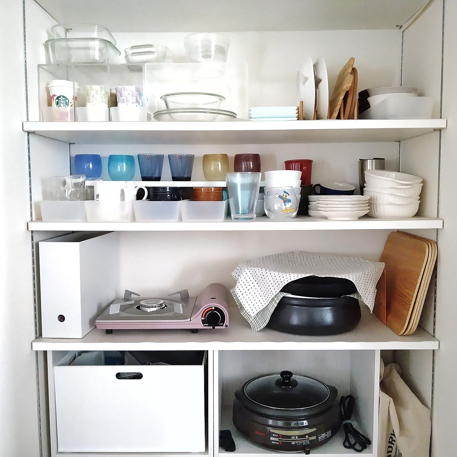 An Iwatani Tatsujin Slim cassette stove stored on a kitchen shelf beside a file box for gas canisters.