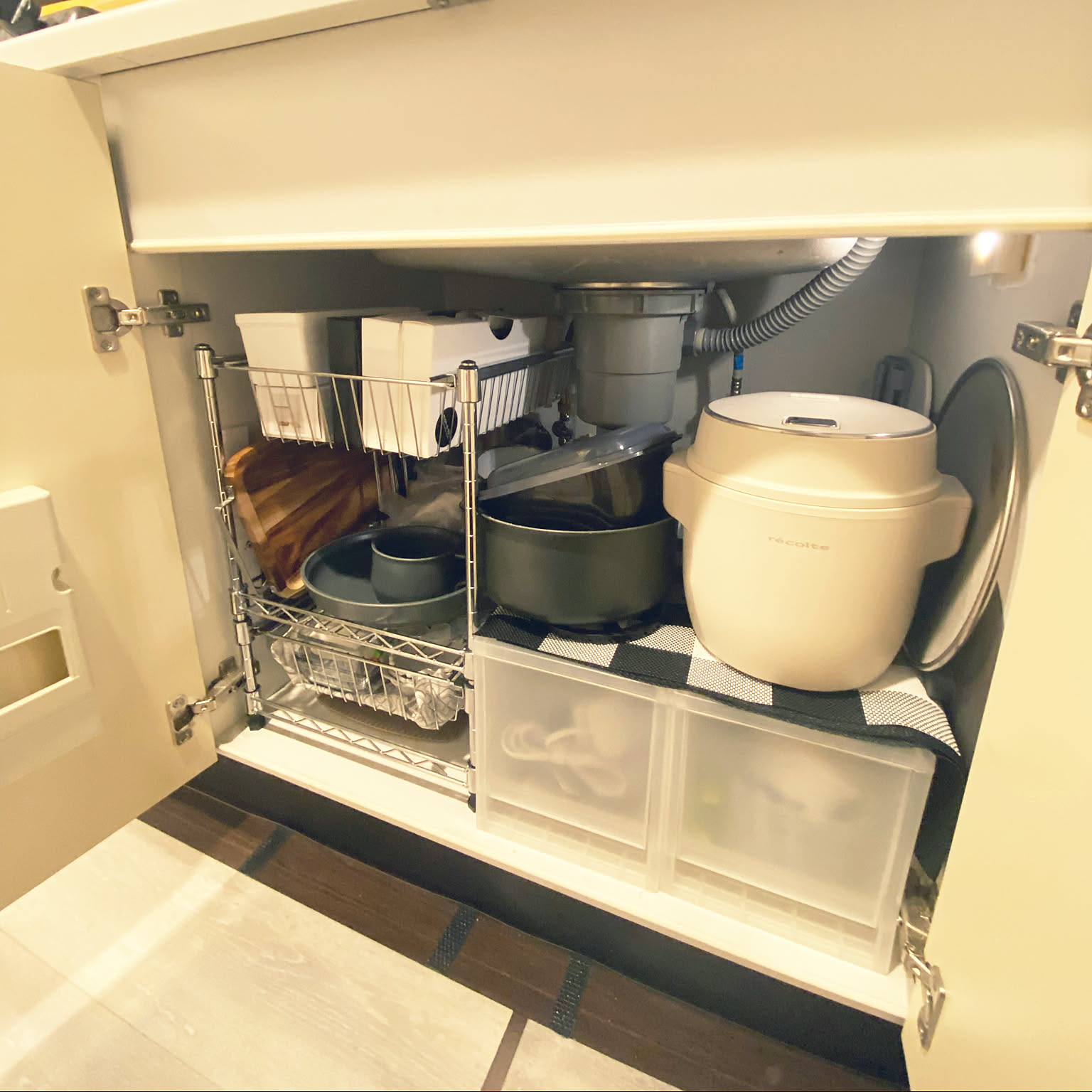 A white Recolte compact rice cooker stored under a kitchen sink with pots and shelves.