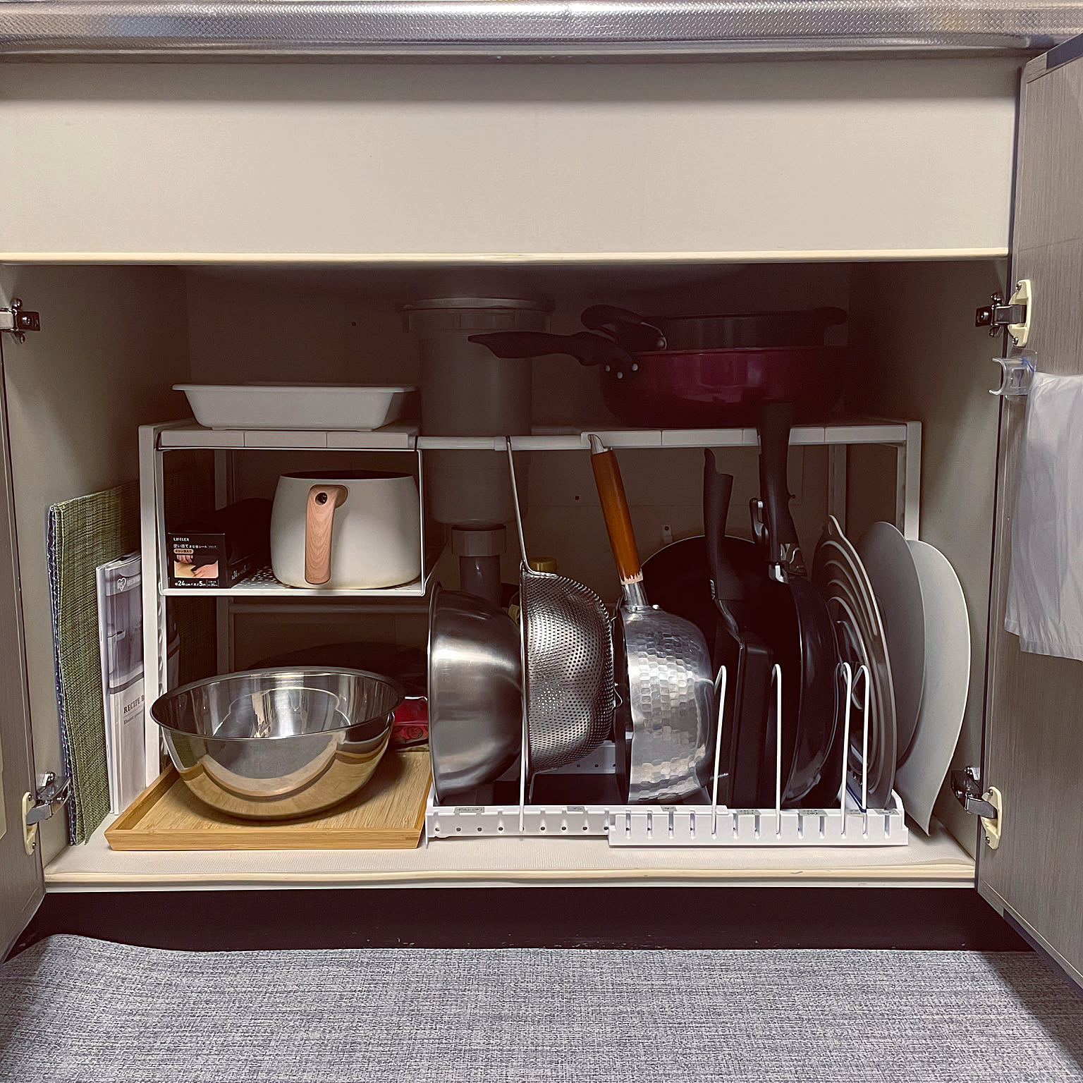An under-sink cabinet organized with adjustable racks, vertical dividers, bowls, pans, lids, trays, and cutting boards.