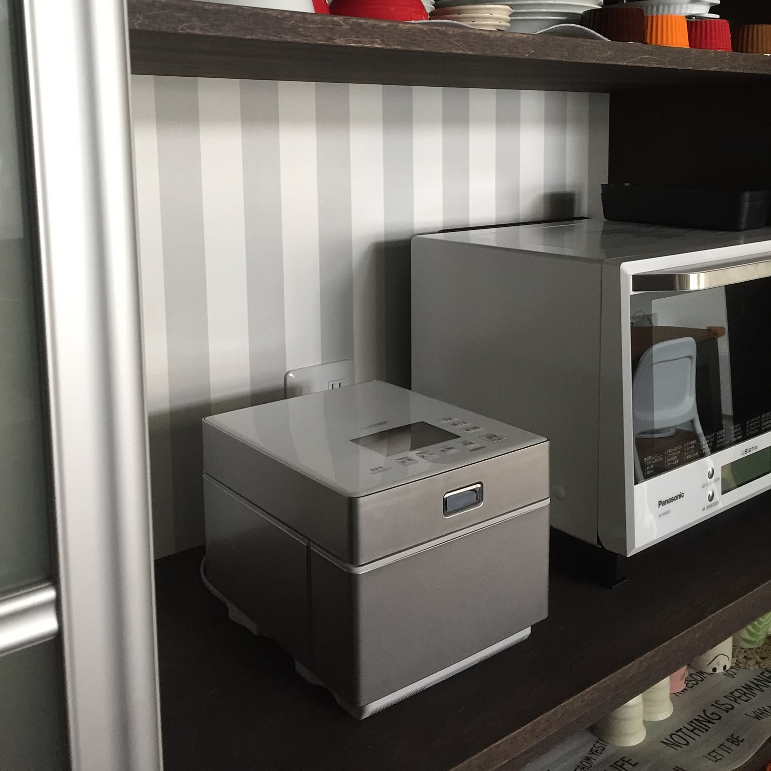 A silver 5.5-cup steamless rice cooker stored neatly on a kitchen shelf beside a microwave.