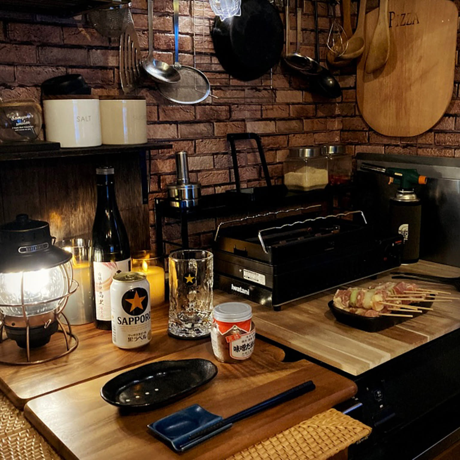 An Iwatani Aburiya II grill staged on a compact counter with skewers and drinks.