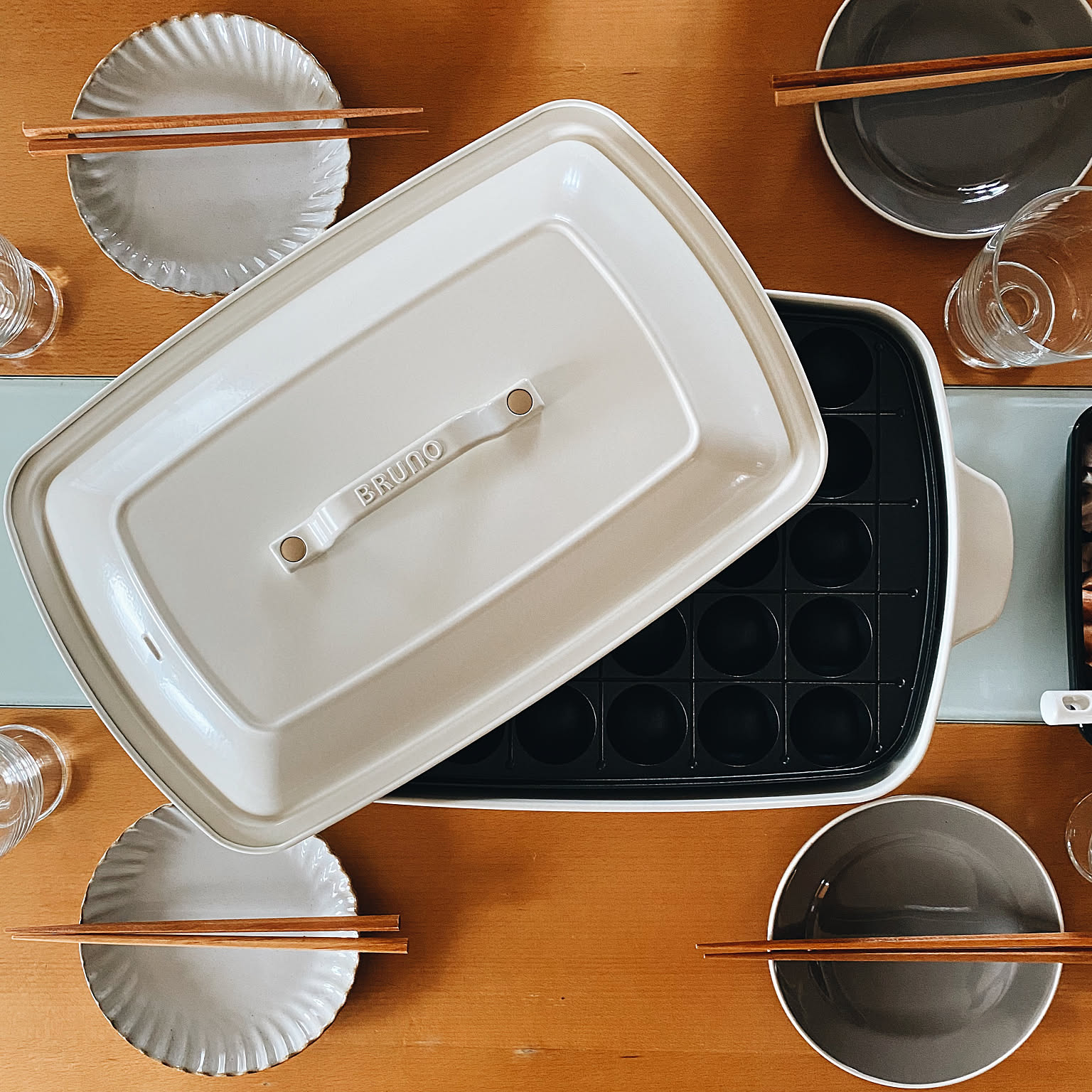 A white BRUNO hot plate with a takoyaki plate set on a dining table.