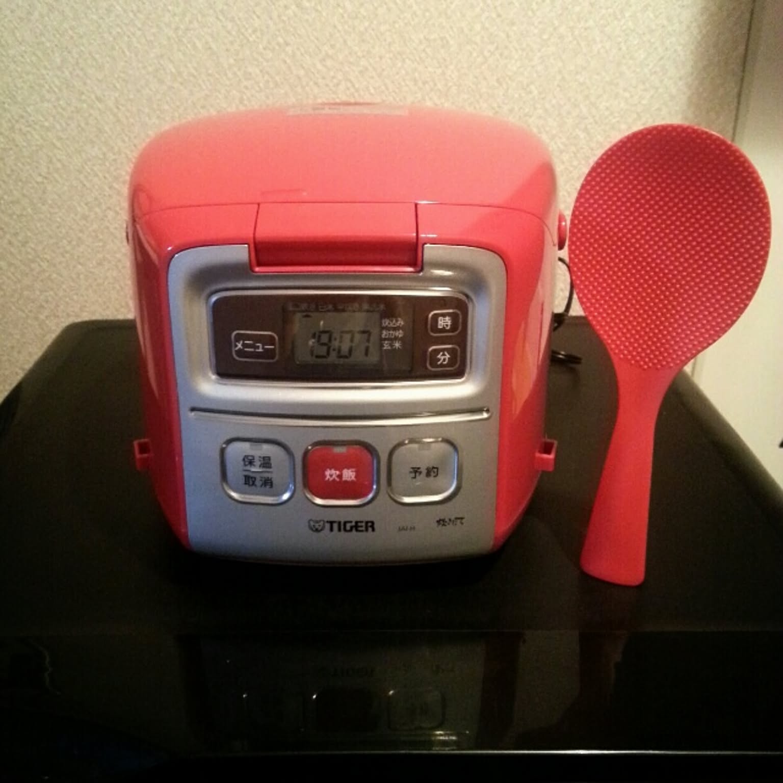 A red Tiger 3-cup micom rice cooker shown beside a matching rice paddle.