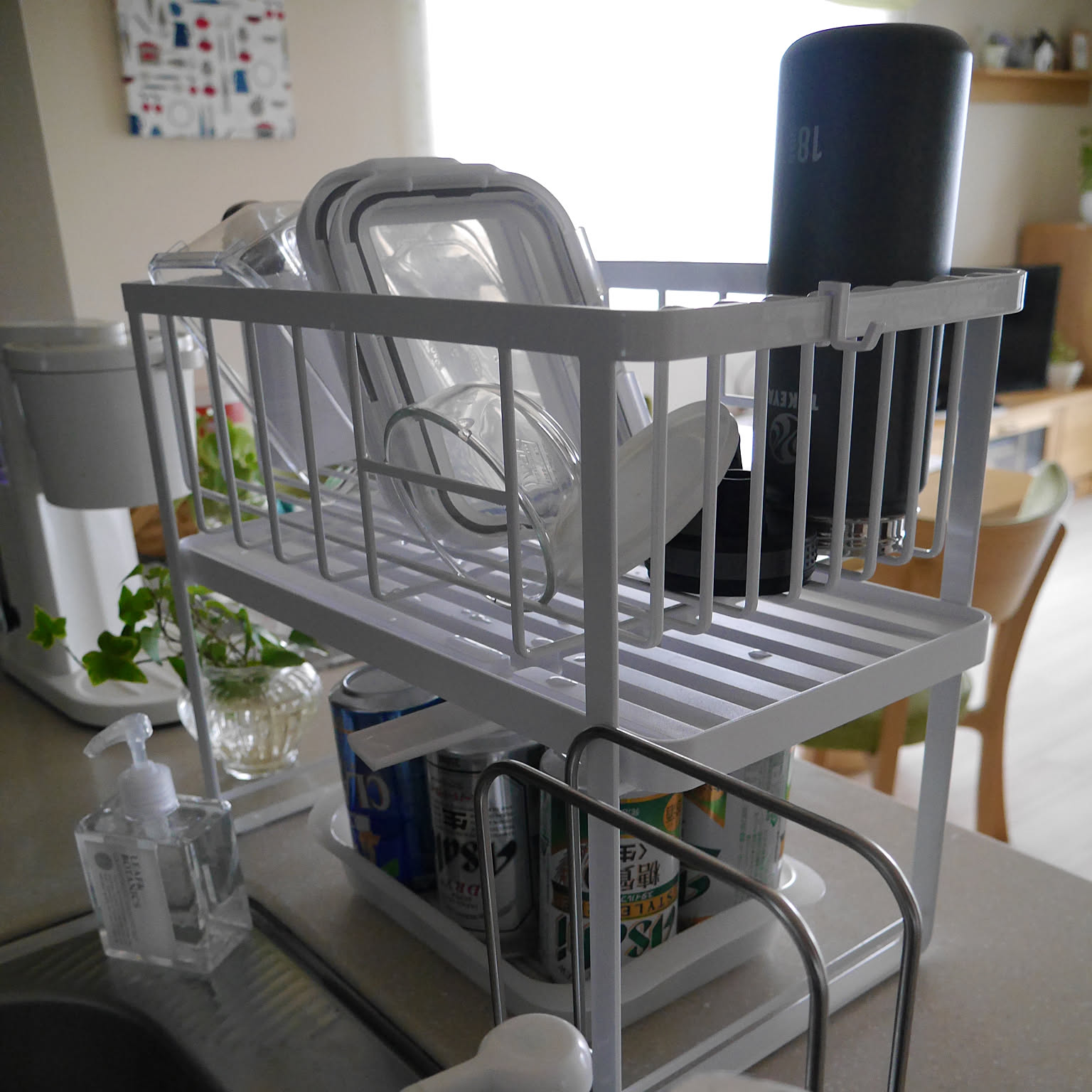 A white Yamazaki Tower two-tier dish rack holding lids, cups, and containers in a bright kitchen.