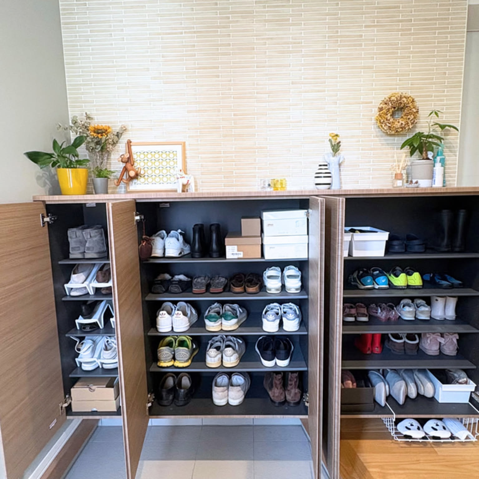 A wide shoe cabinet opened to show many pairs arranged by shelf in a Japanese entryway.