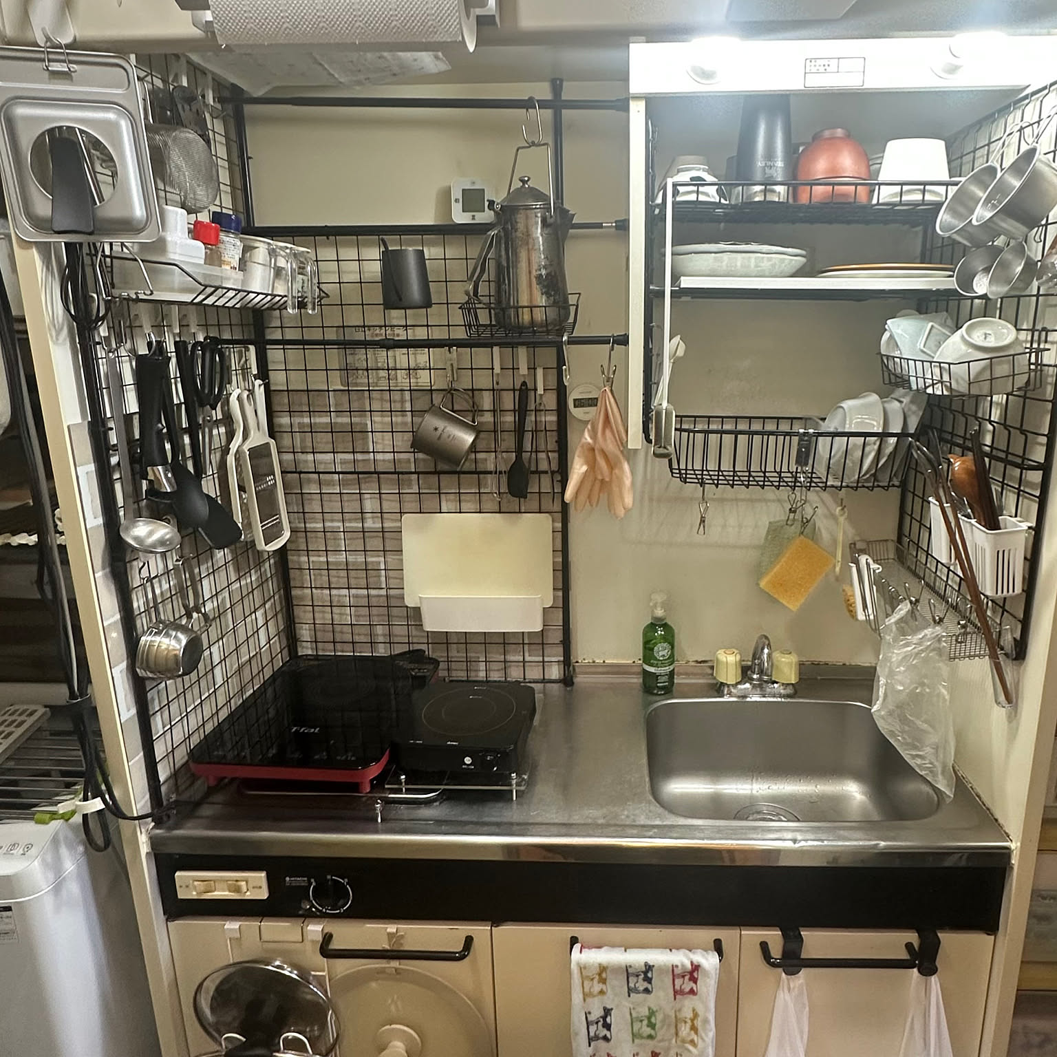 A 1K Japanese apartment mini kitchen using tension rods and wire panels for wall storage above the sink and cooktop.
