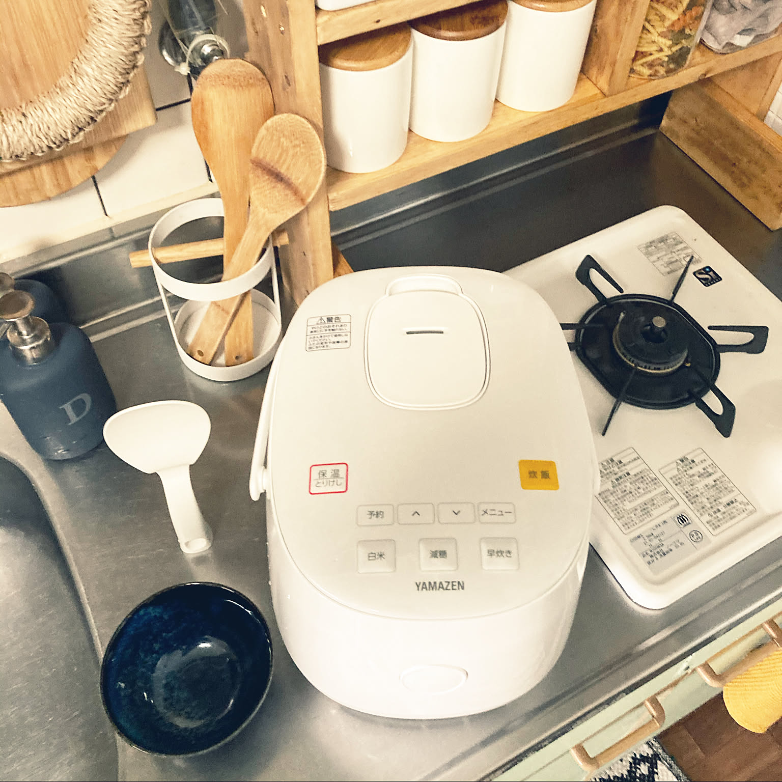 A white Yamazen rice cooker set beside a gas stove in a narrow kitchen.