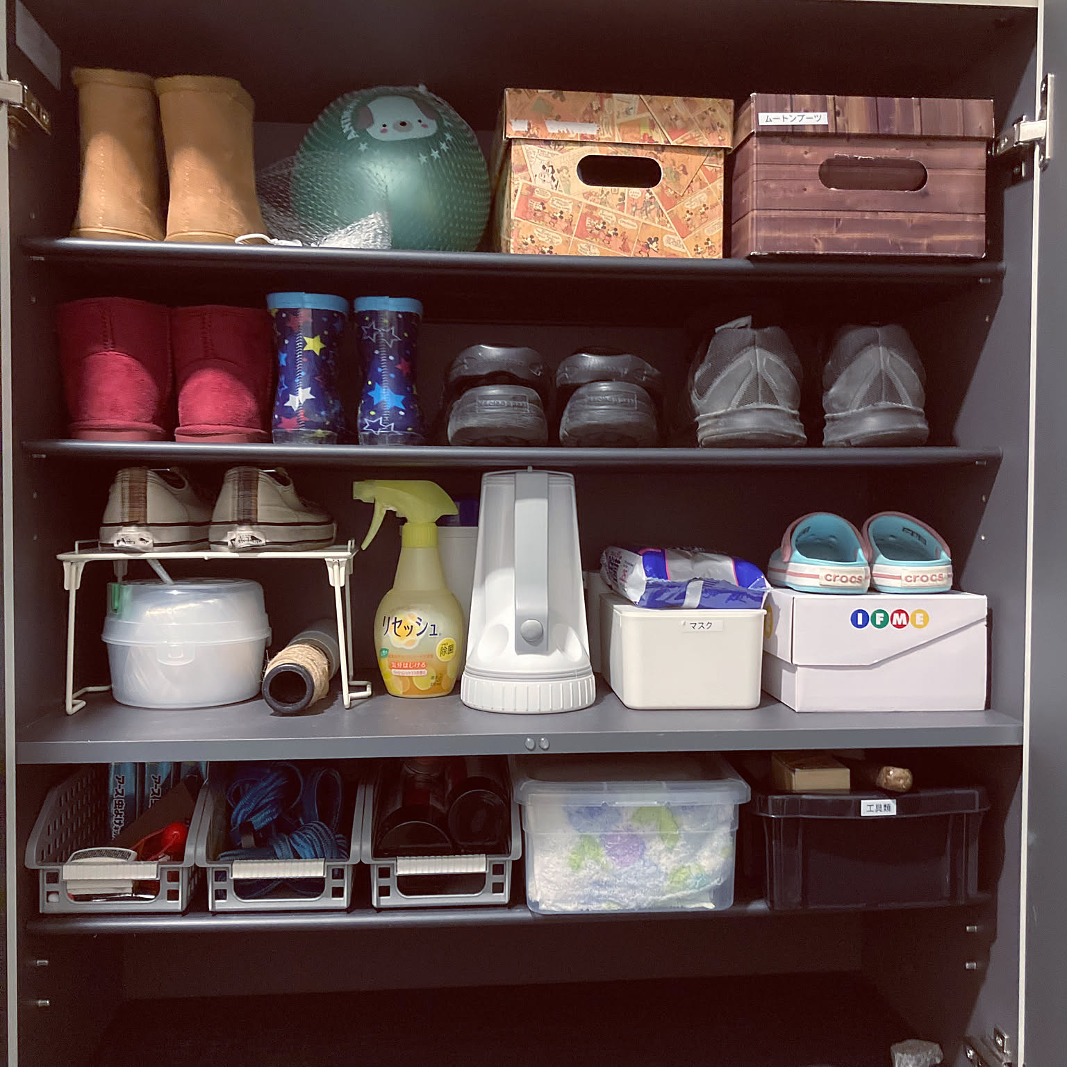 An organized Japanese shoe cabinet with shoes, storage boxes, rain gear, and daily supplies arranged by shelf.