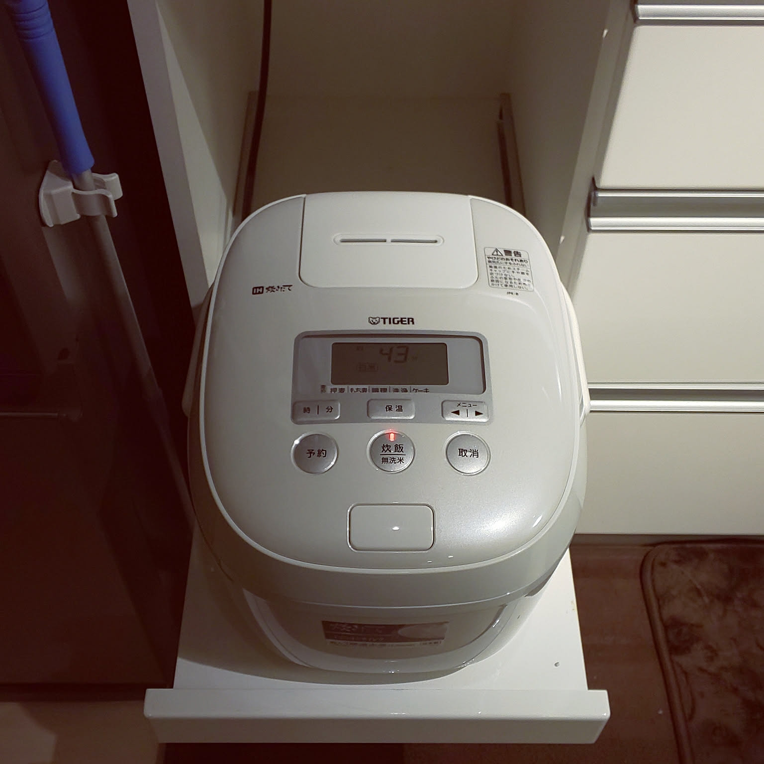 A pearl white Tiger rice cooker fitted tightly into a compact kitchen appliance space.