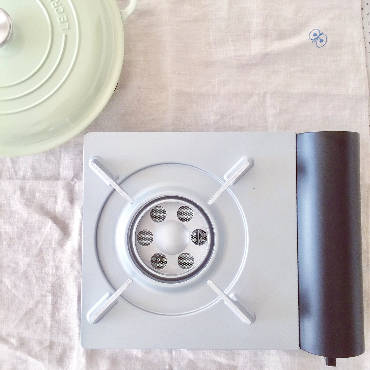 An Iwatani Eco Premium cassette stove viewed from above beside a pot lid.