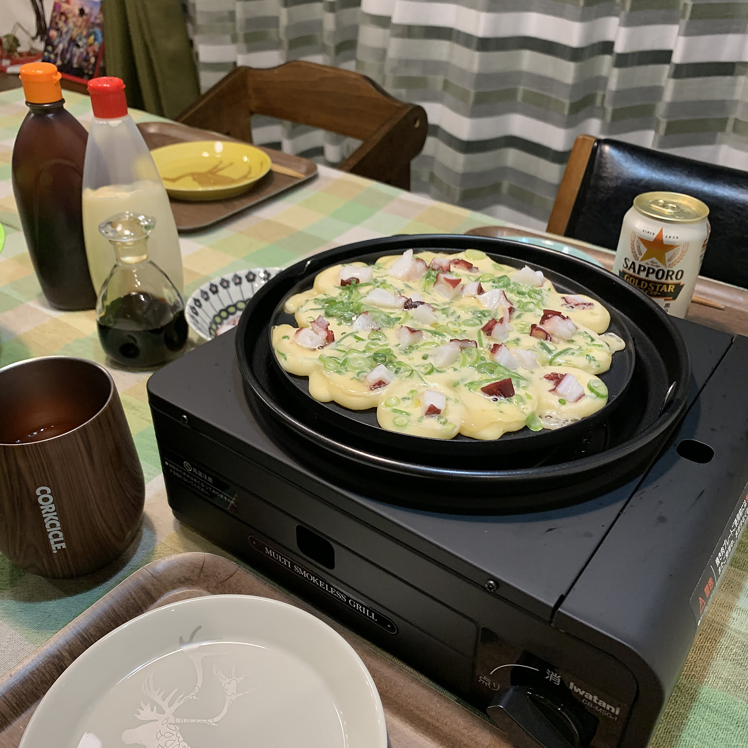 A black Iwatani gas-powered takoyaki grill cooking batter on a dining table.