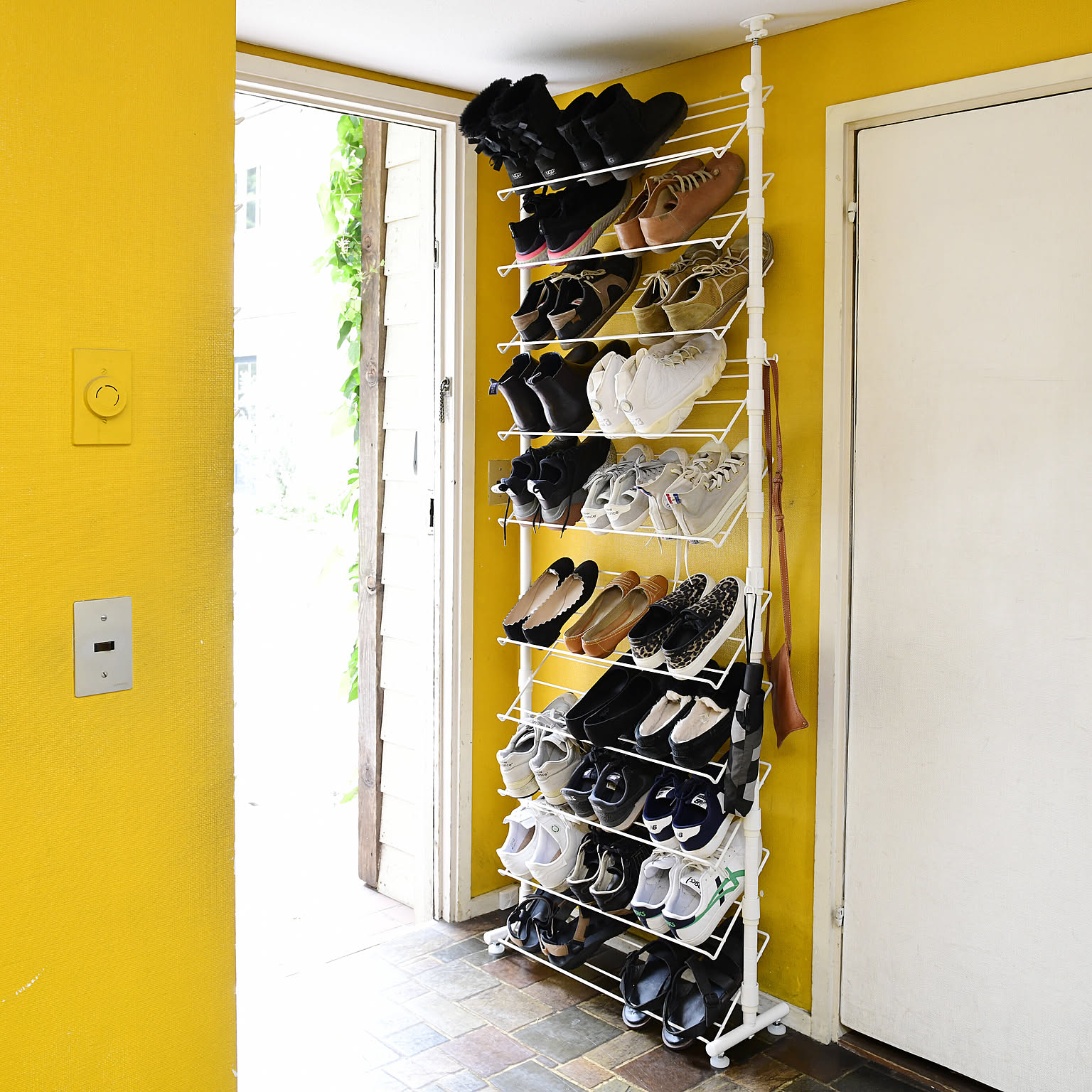 A tall narrow shoe rack filled with sneakers and shoes beside a front door.