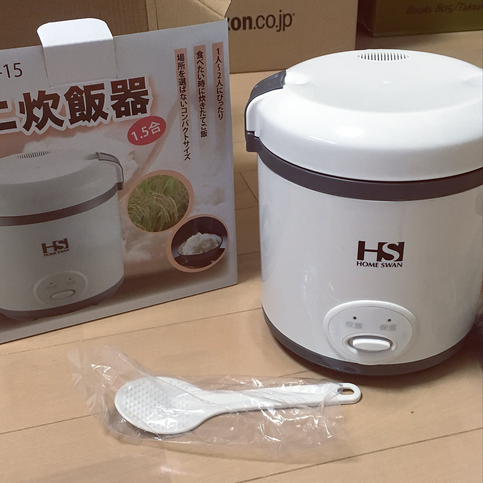 A white 1.5-cup Home Swan mini rice cooker beside its box and rice paddle.