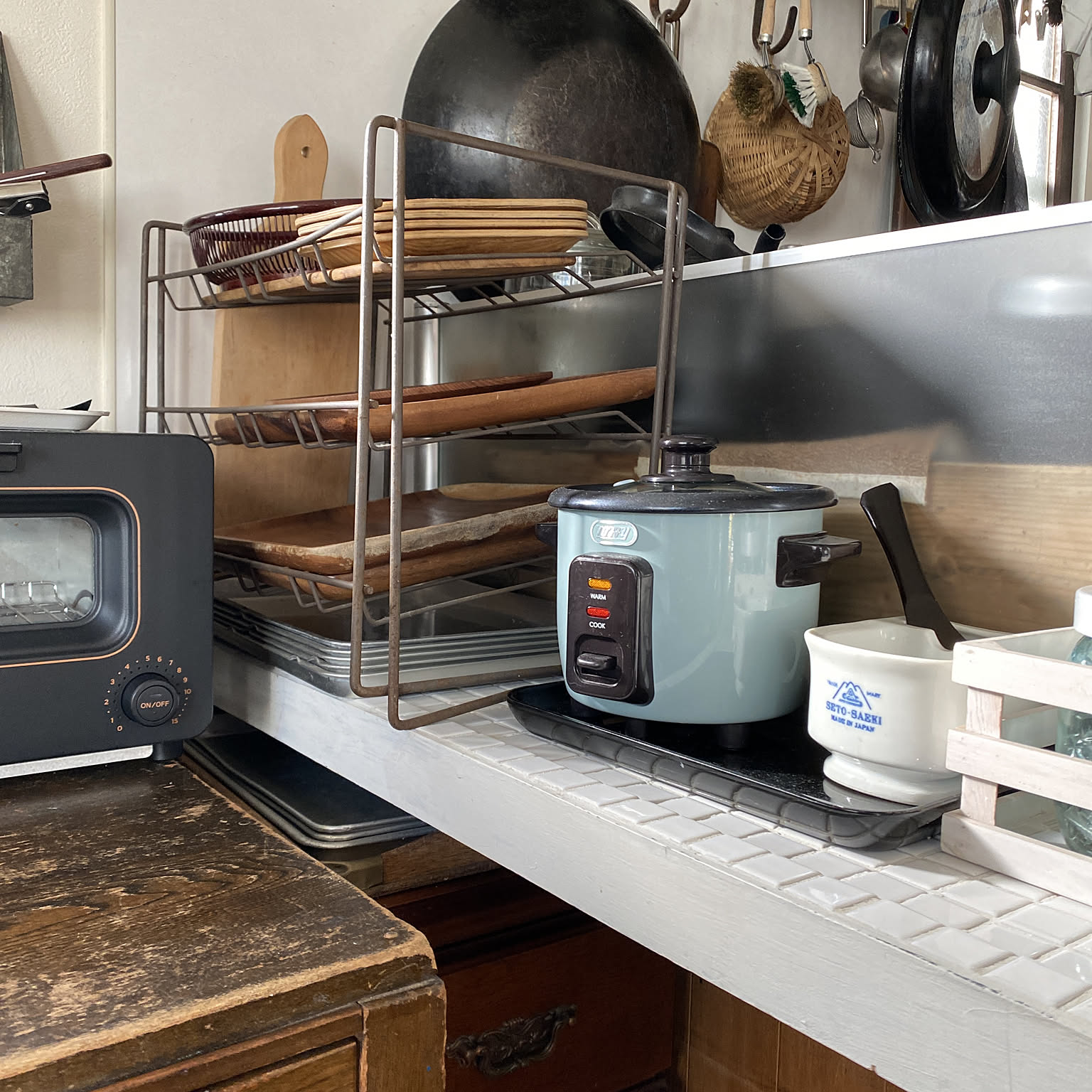 A small blue rice cooker placed on a narrow kitchen counter beside a toaster and dish rack.