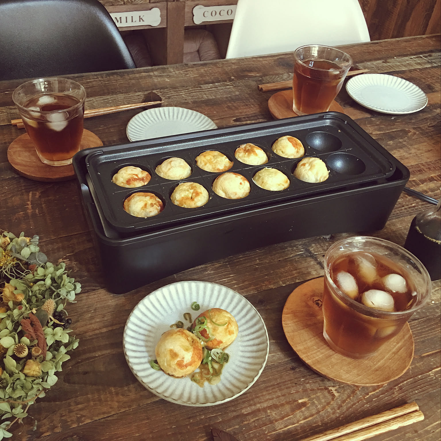 A slim electric takoyaki maker cooking takoyaki on a narrow dining table.