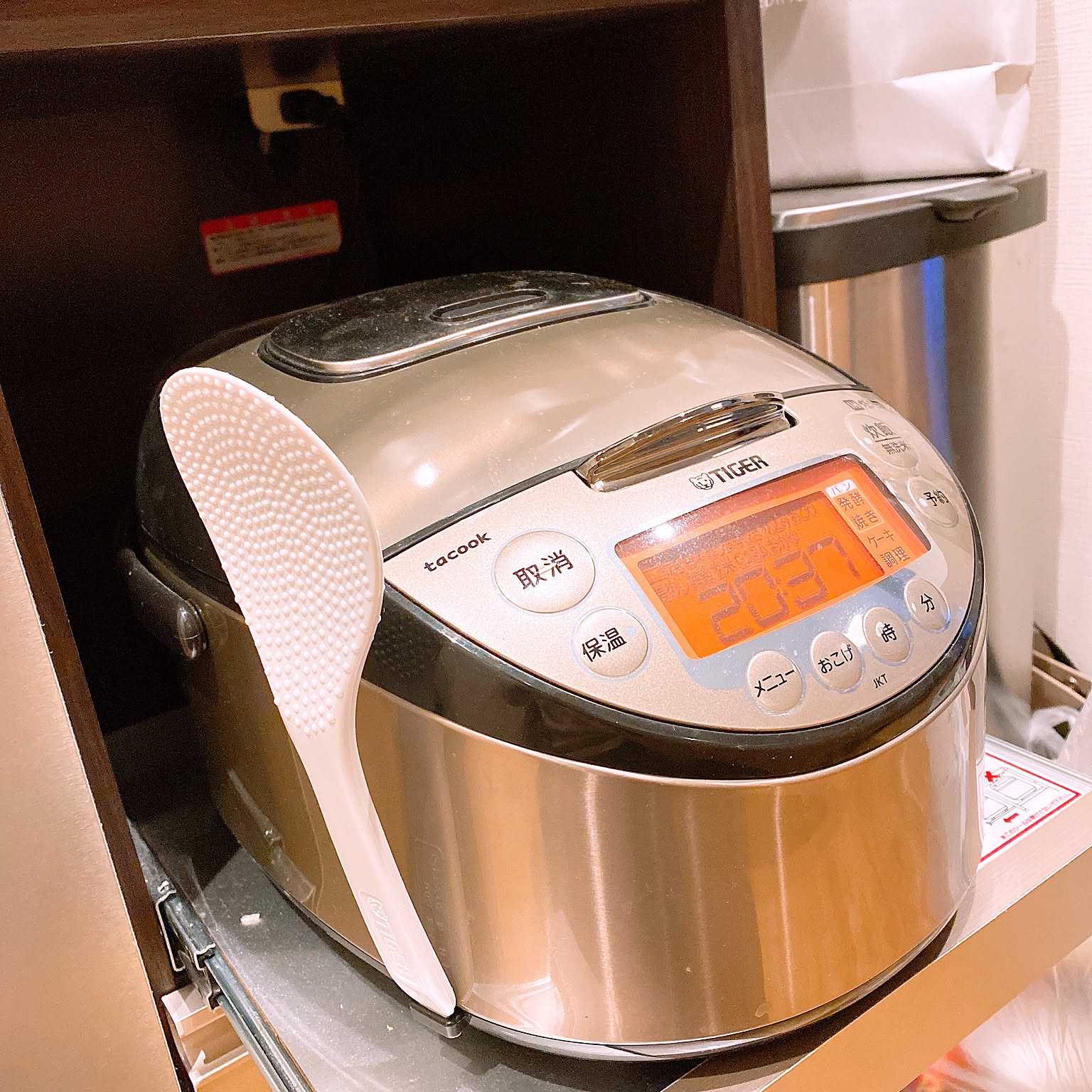 A brown Tiger tacook IH rice cooker shown close-up in a kitchen cabinet.