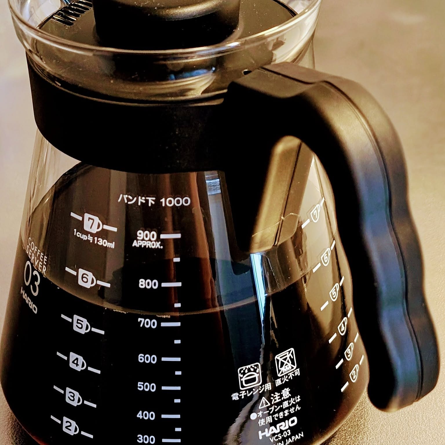 A close-up of a black HARIO V60 coffee server with measurement marks and a large handle.