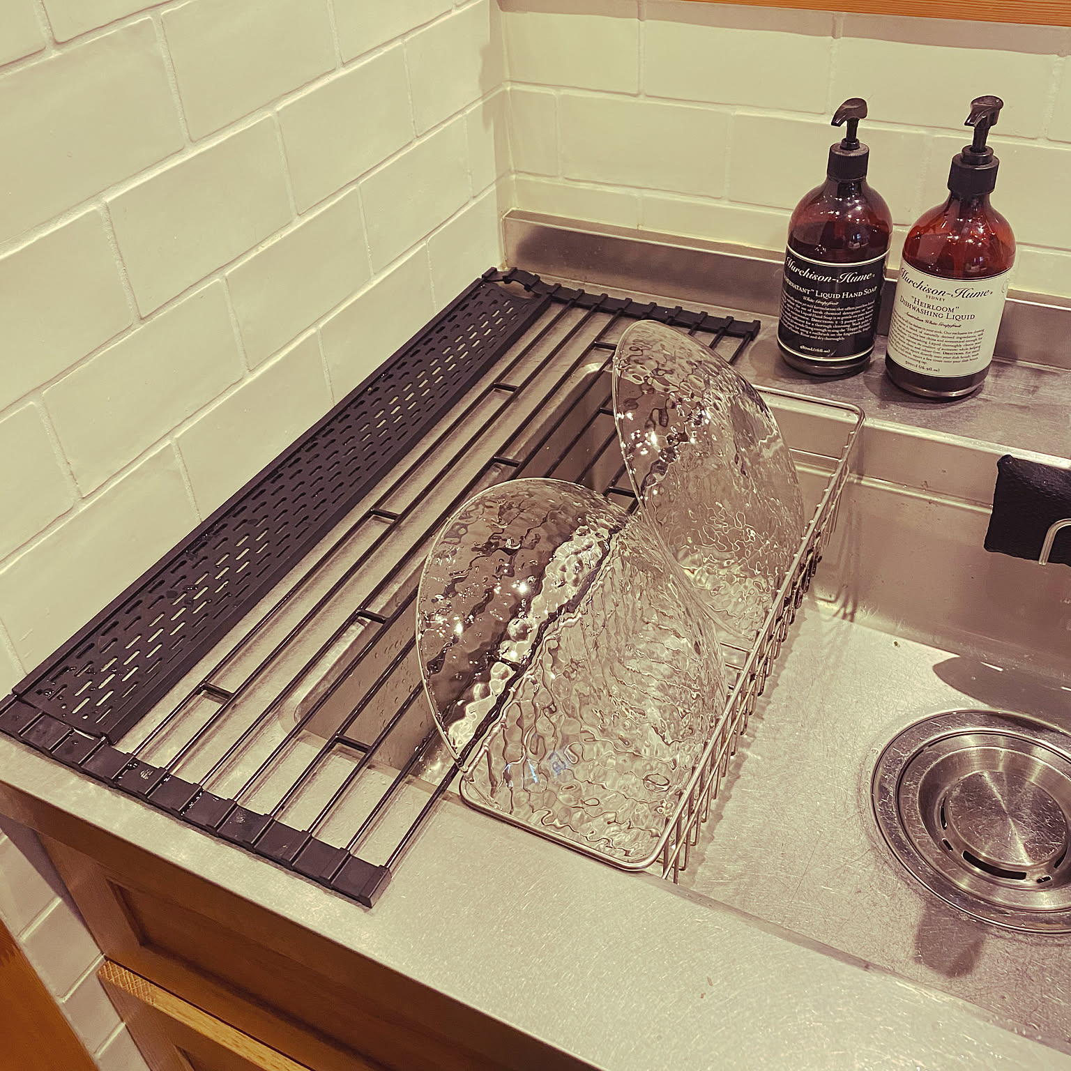 A white Yamazaki folding drainer with a silicone tray holding glasses and small items above a sink.