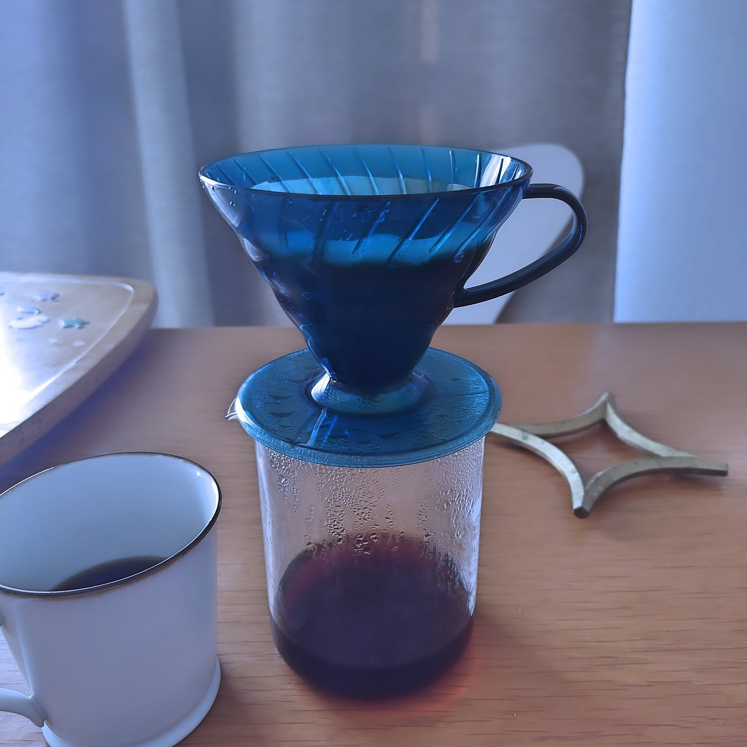 A blue HARIO V60 01 ceramic dripper placed on a glass server beside a mug.