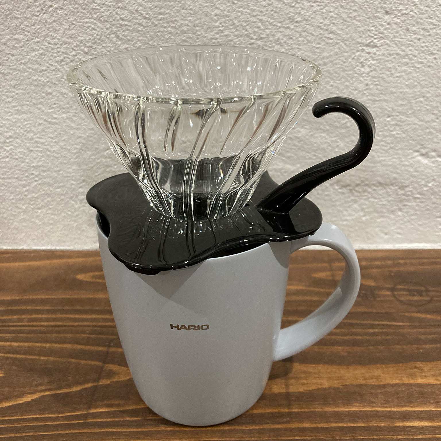 A HARIO heatproof glass V60 dripper with a black handle sitting on a white mug.
