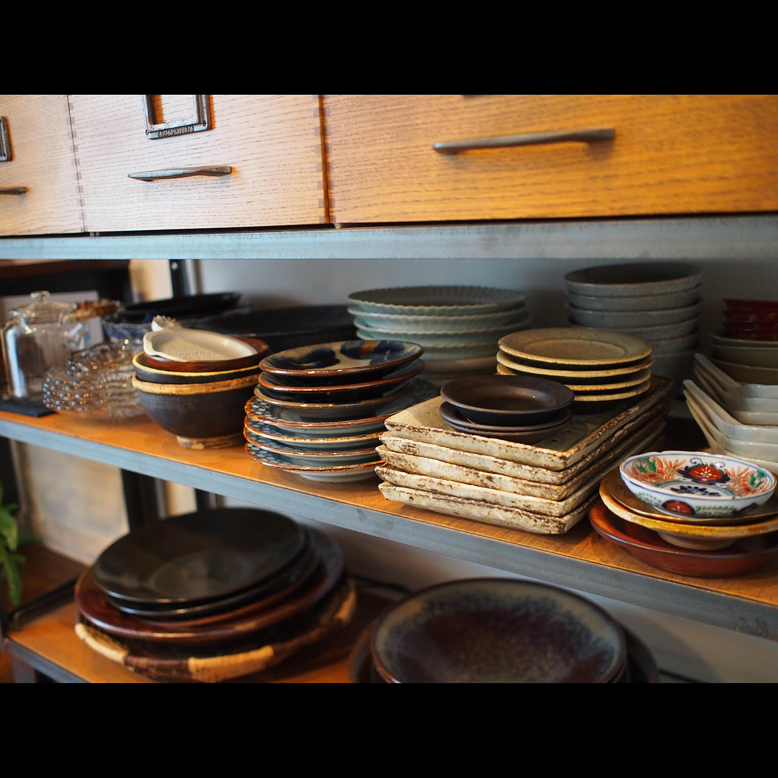 Open shelf storing stacks of Japanese bowls, plates, and serving dishes.