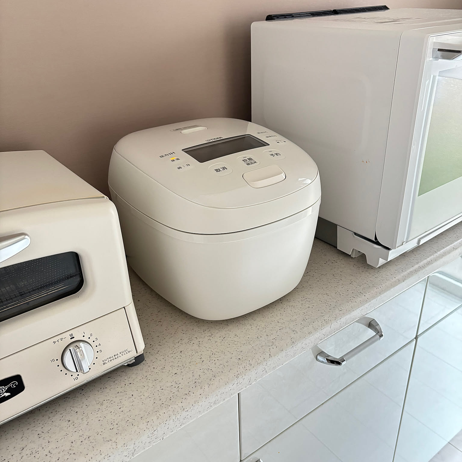 A white Tiger pressure IH rice cooker shown clearly between white kitchen appliances.