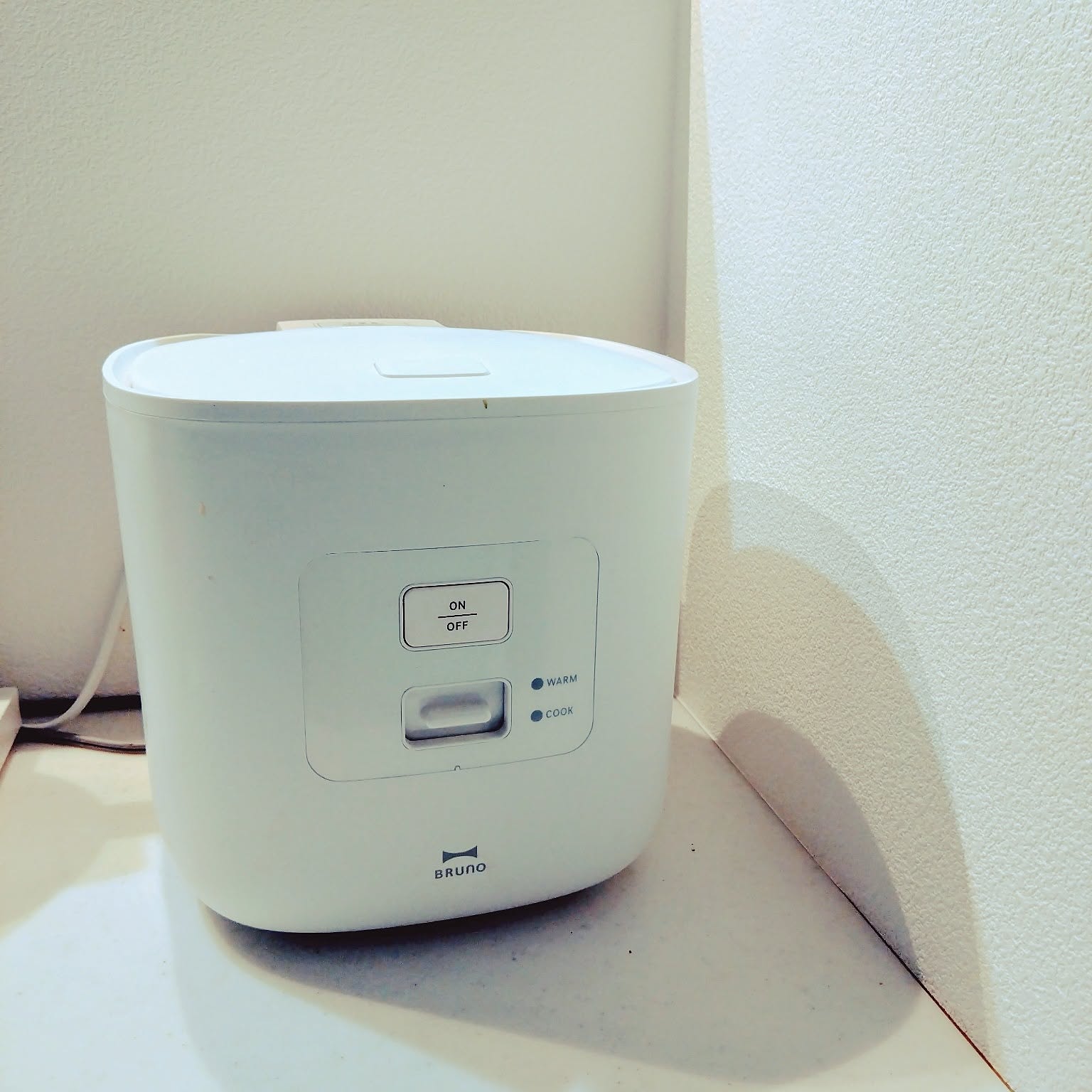 A white Bruno three-cup rice cooker set neatly in a kitchen corner.