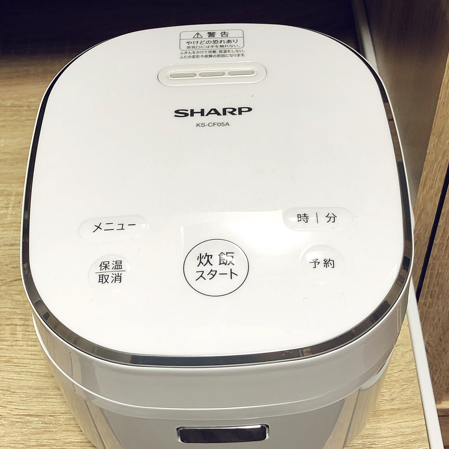 A white Sharp three-cup rice cooker shown close-up with simple top controls.